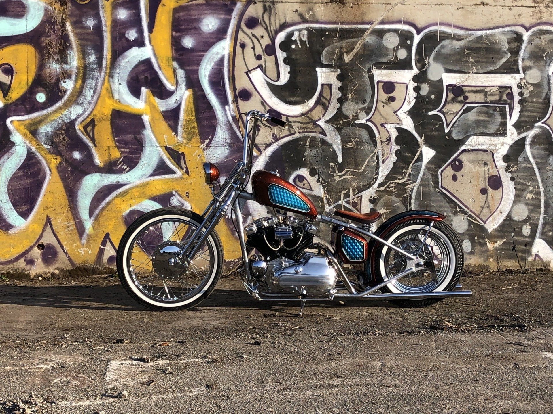 Custom chopper motorcycle parked beside a colorful graffiti wall on a gravel lot