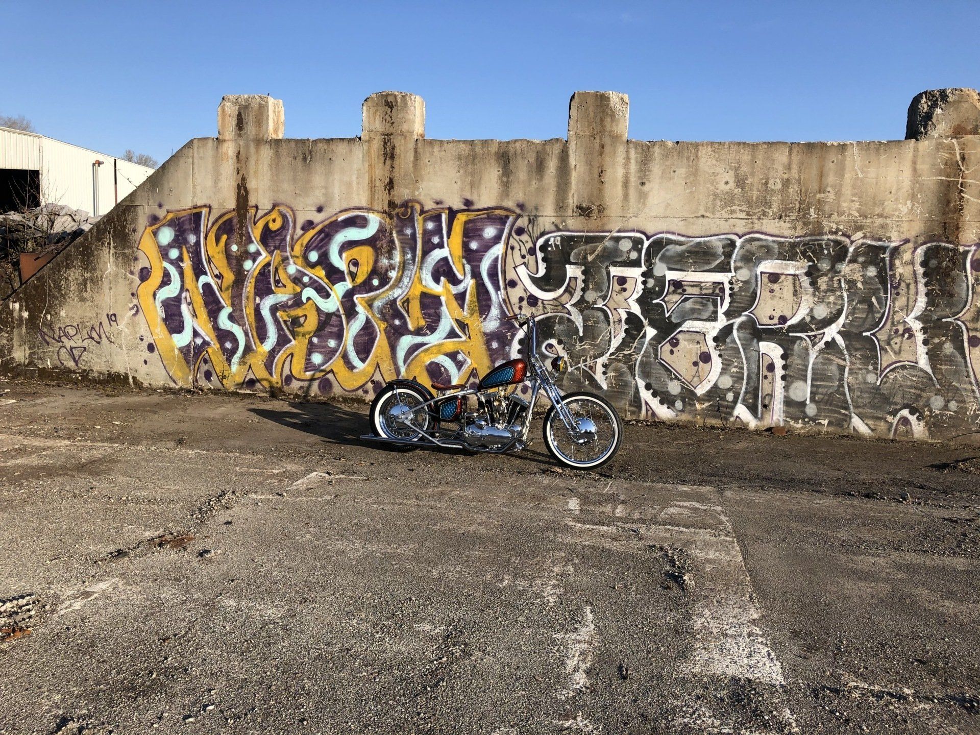 Motorcycle parked beside a graffiti-covered concrete wall in a dusty lot