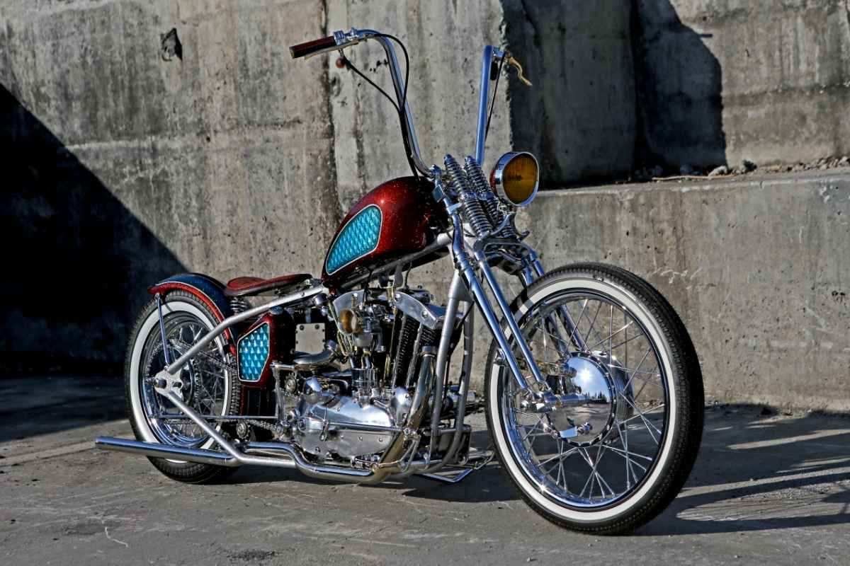 Custom chrome chopper motorcycle with a red-and-teal tank parked against a concrete wall