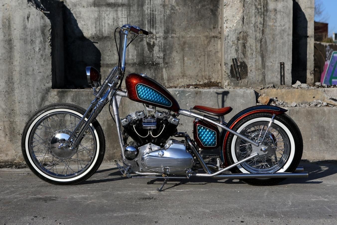 Custom chopper motorcycle with red-and-blue paint parked on a street beside a concrete wall.