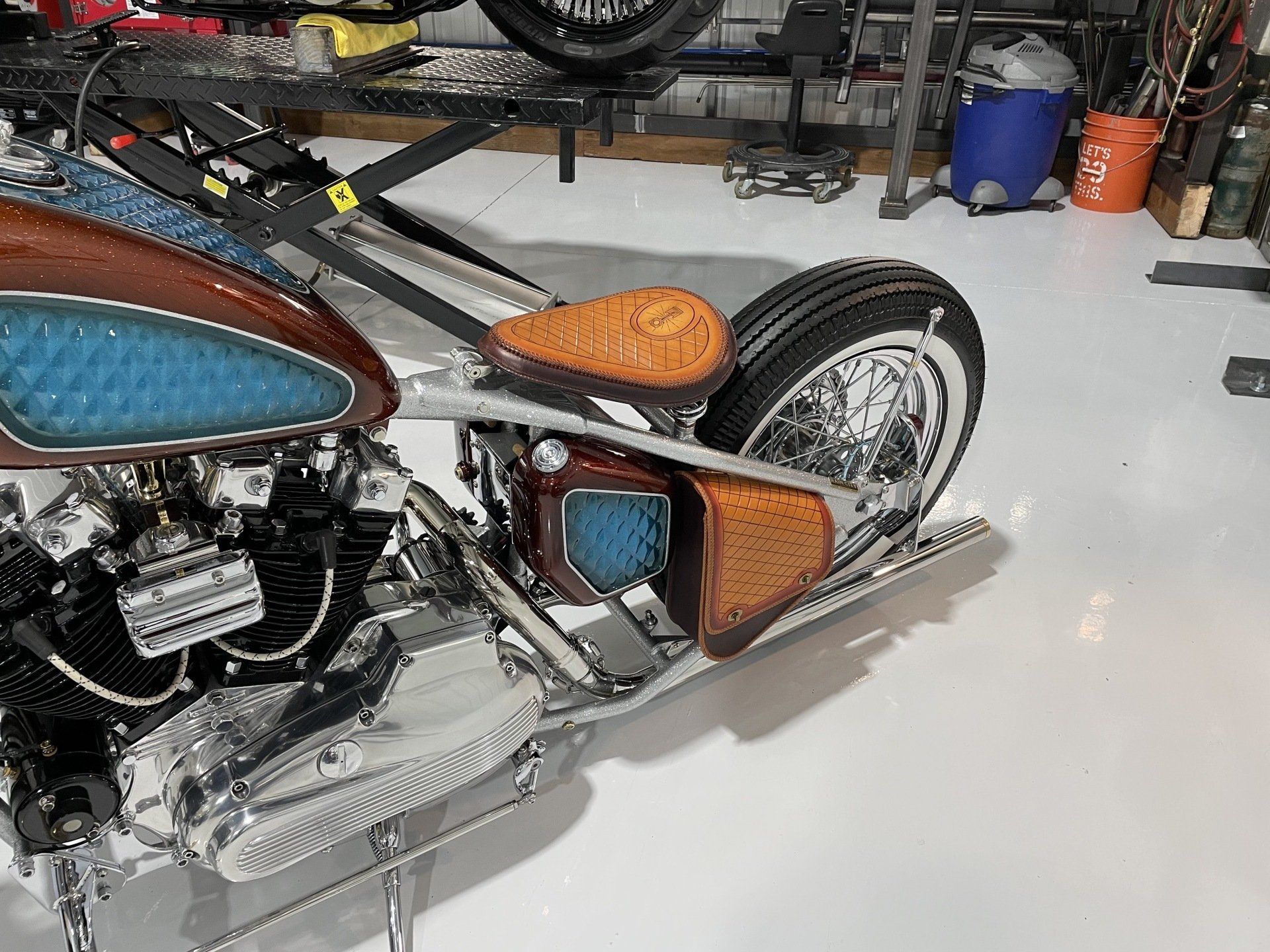 Custom chopper motorcycle in a garage, with blue and orange accents and a large rear wheel