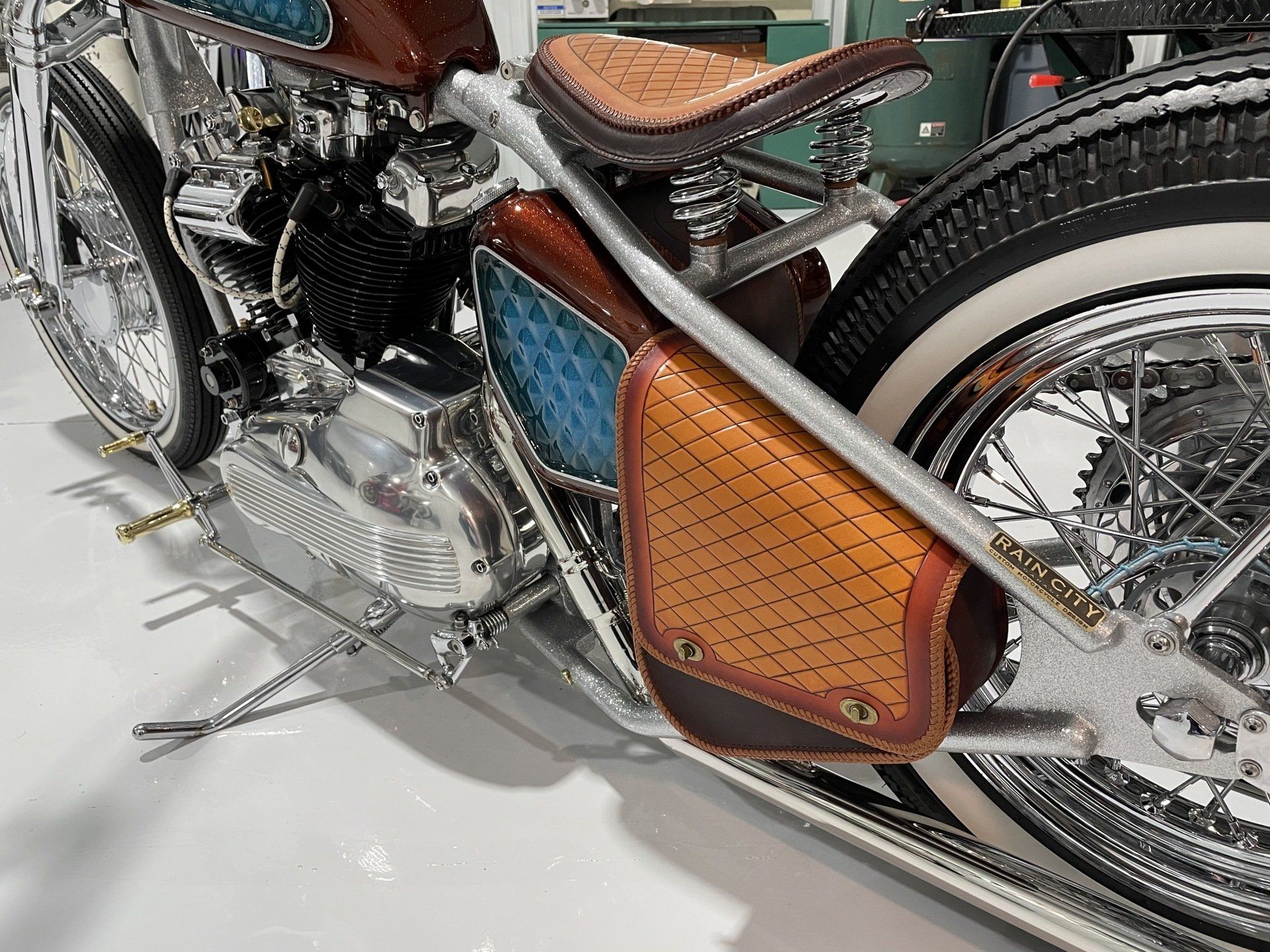 Custom vintage motorcycle with chrome engine and brown leather side panel on a white display floor