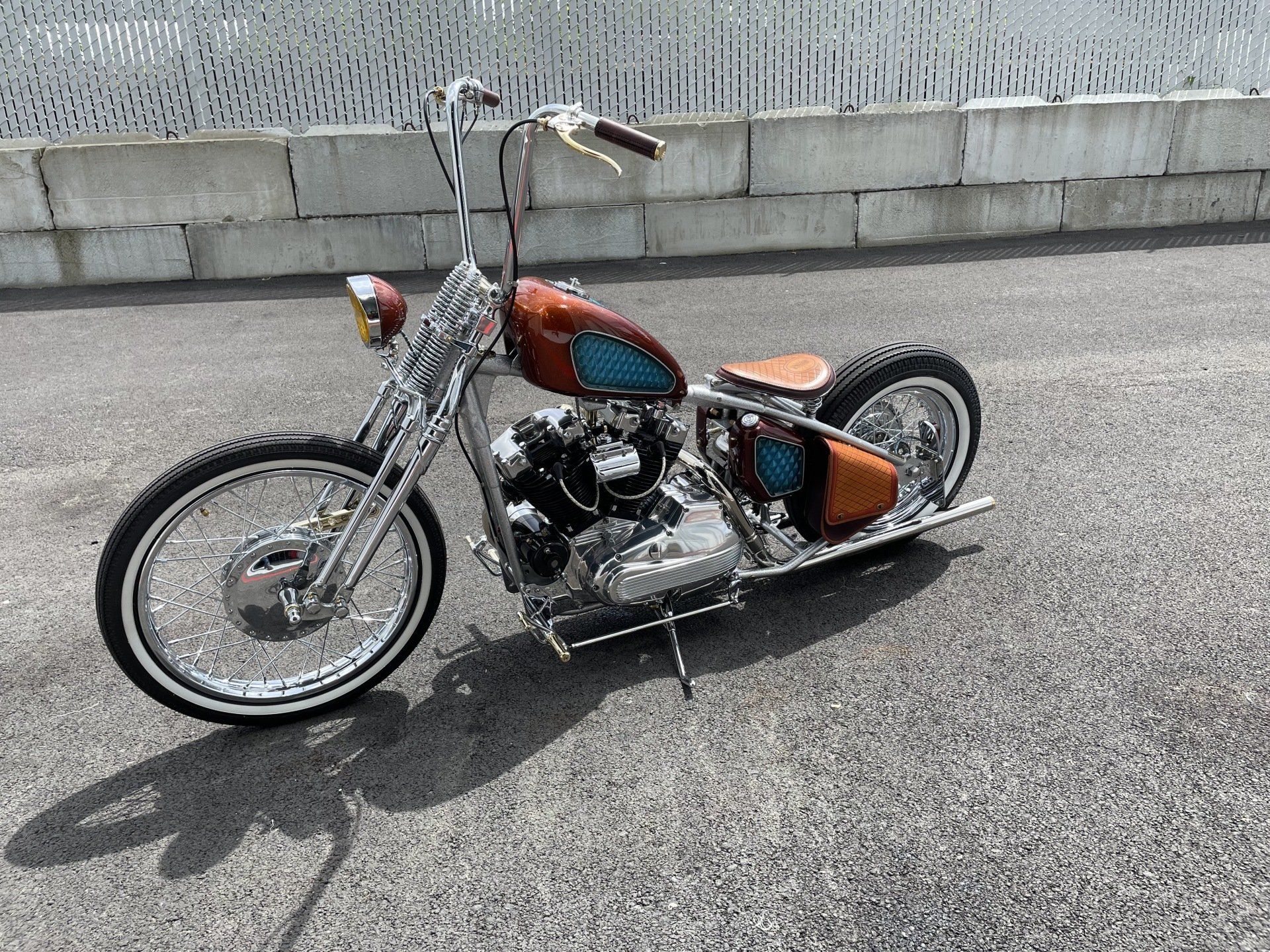 Custom orange and chrome chopper motorcycle parked on asphalt beside a concrete wall
