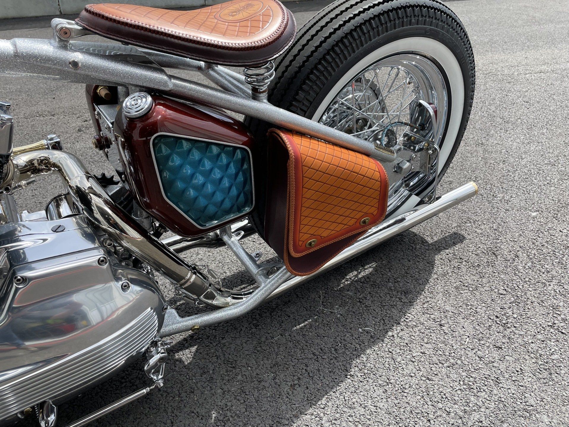 Custom motorcycle close-up with chrome engine, brown seat, and colorful side covers on pavement
