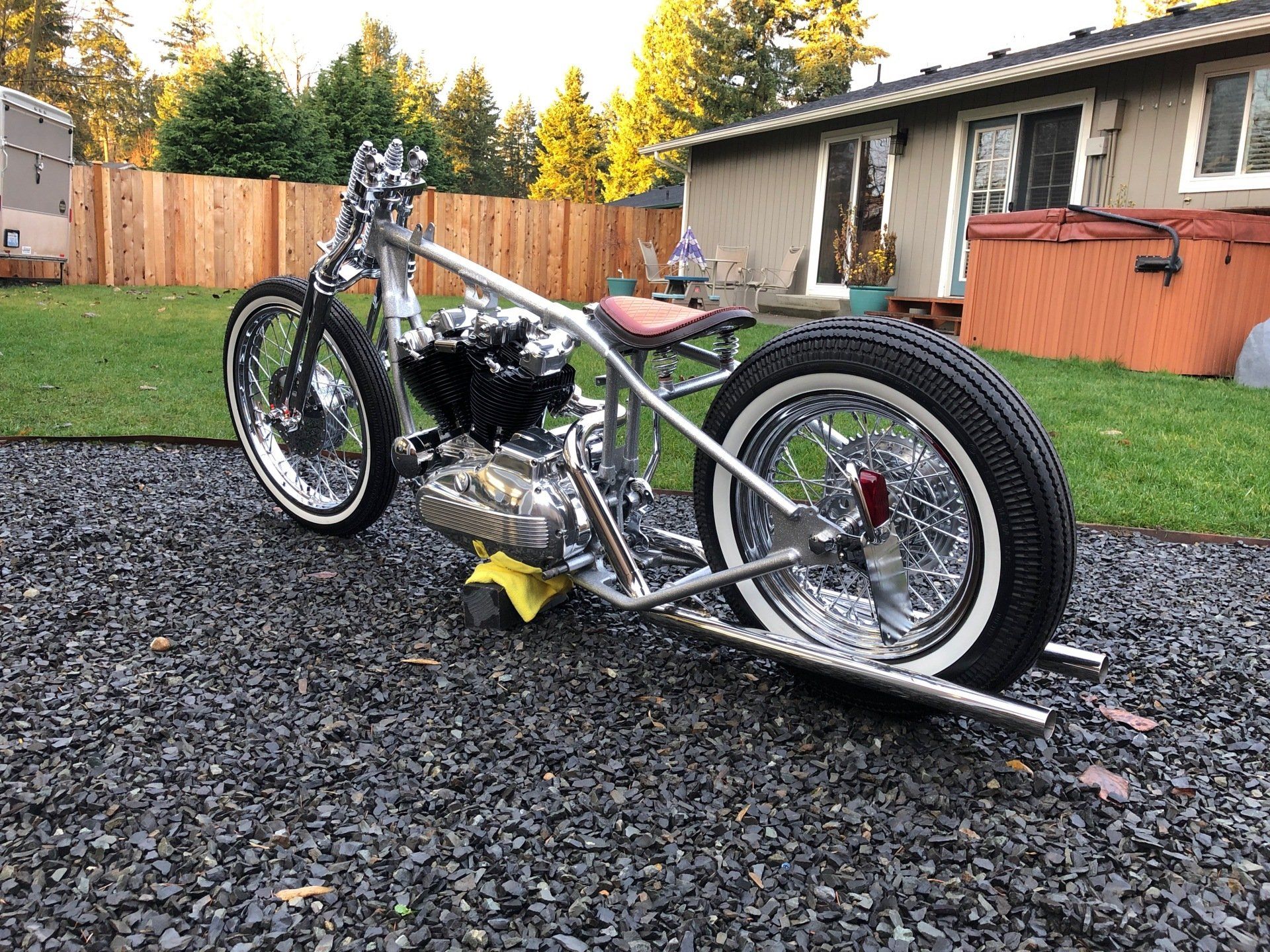 Custom lowrider-style motorcycle on gravel in a suburban yard, with fence and house in the background