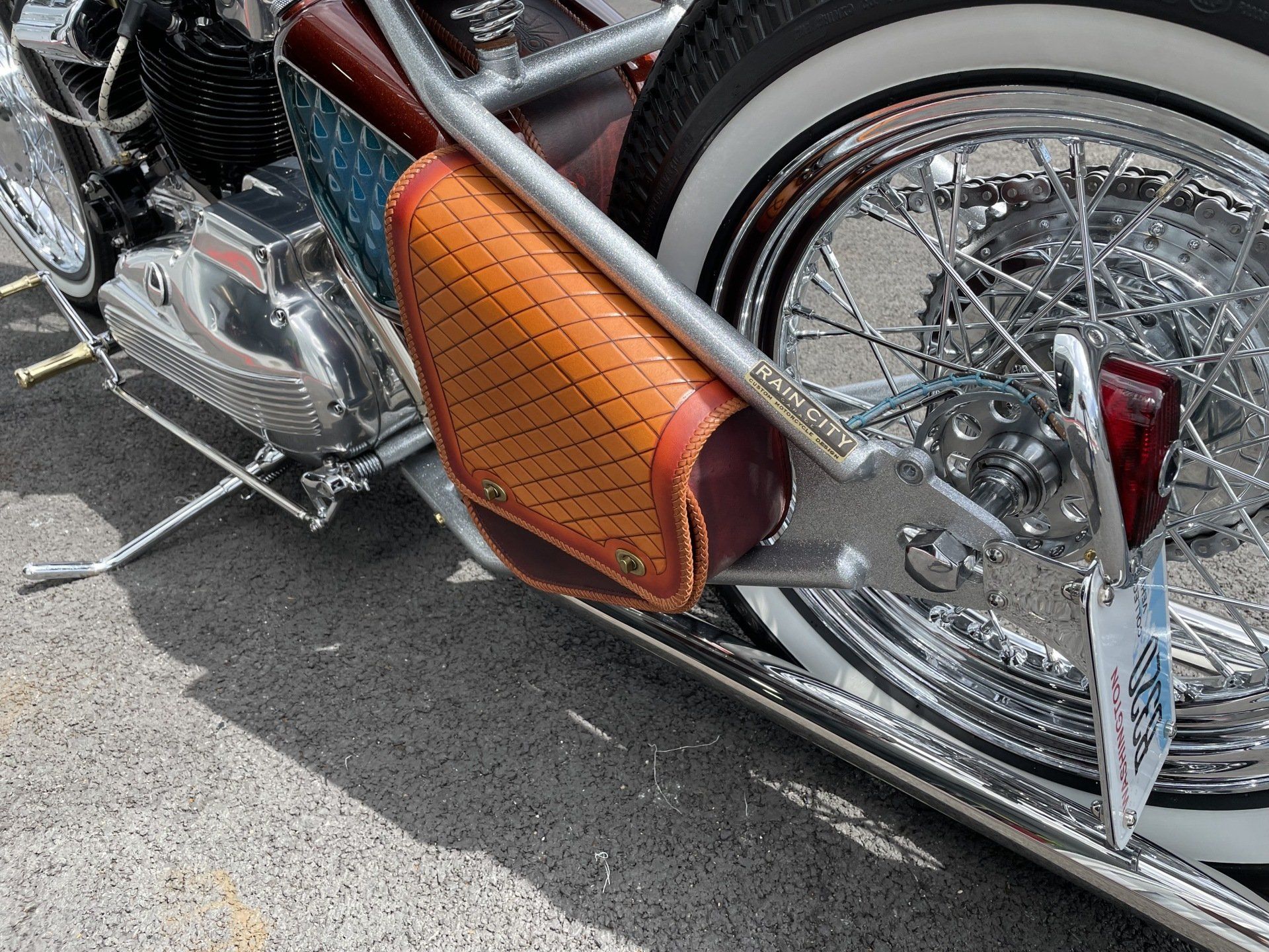 Chrome motorcycle with orange leather side bag and a spoked rear wheel on pavement
