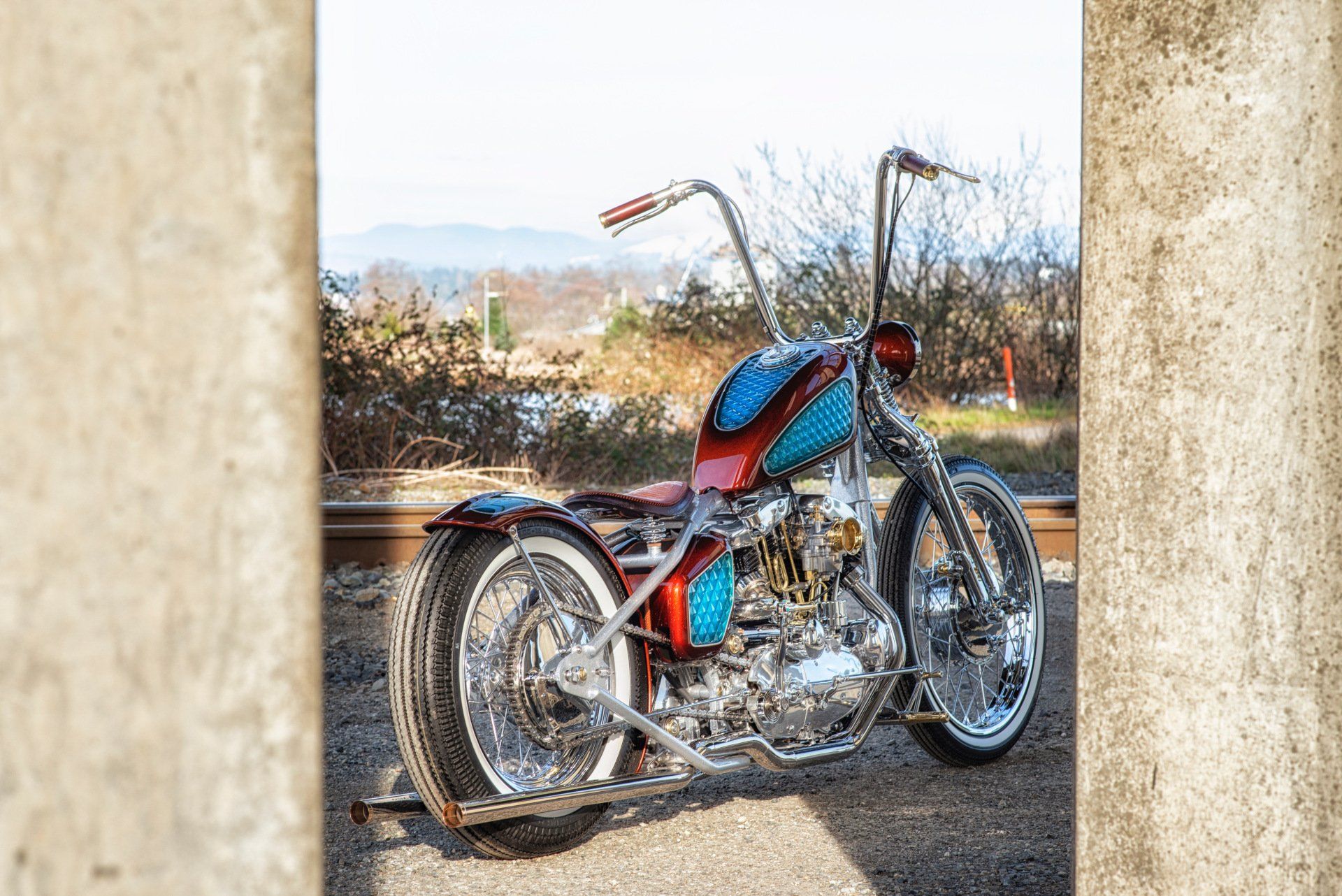Custom red-and-blue motorcycle parked outdoors between stone pillars