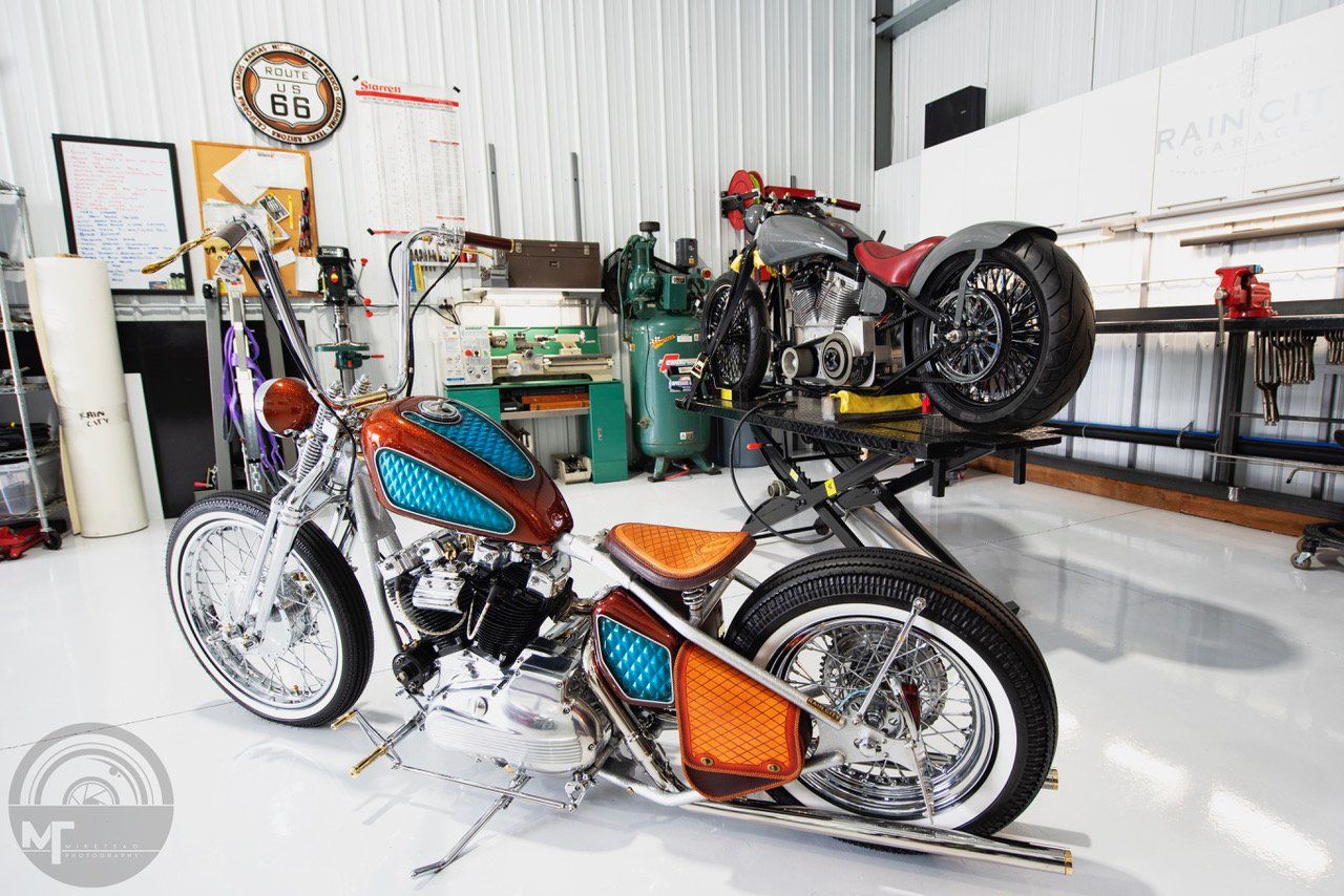 Custom chopper motorcycle with blue and orange paint in a bright garage workshop