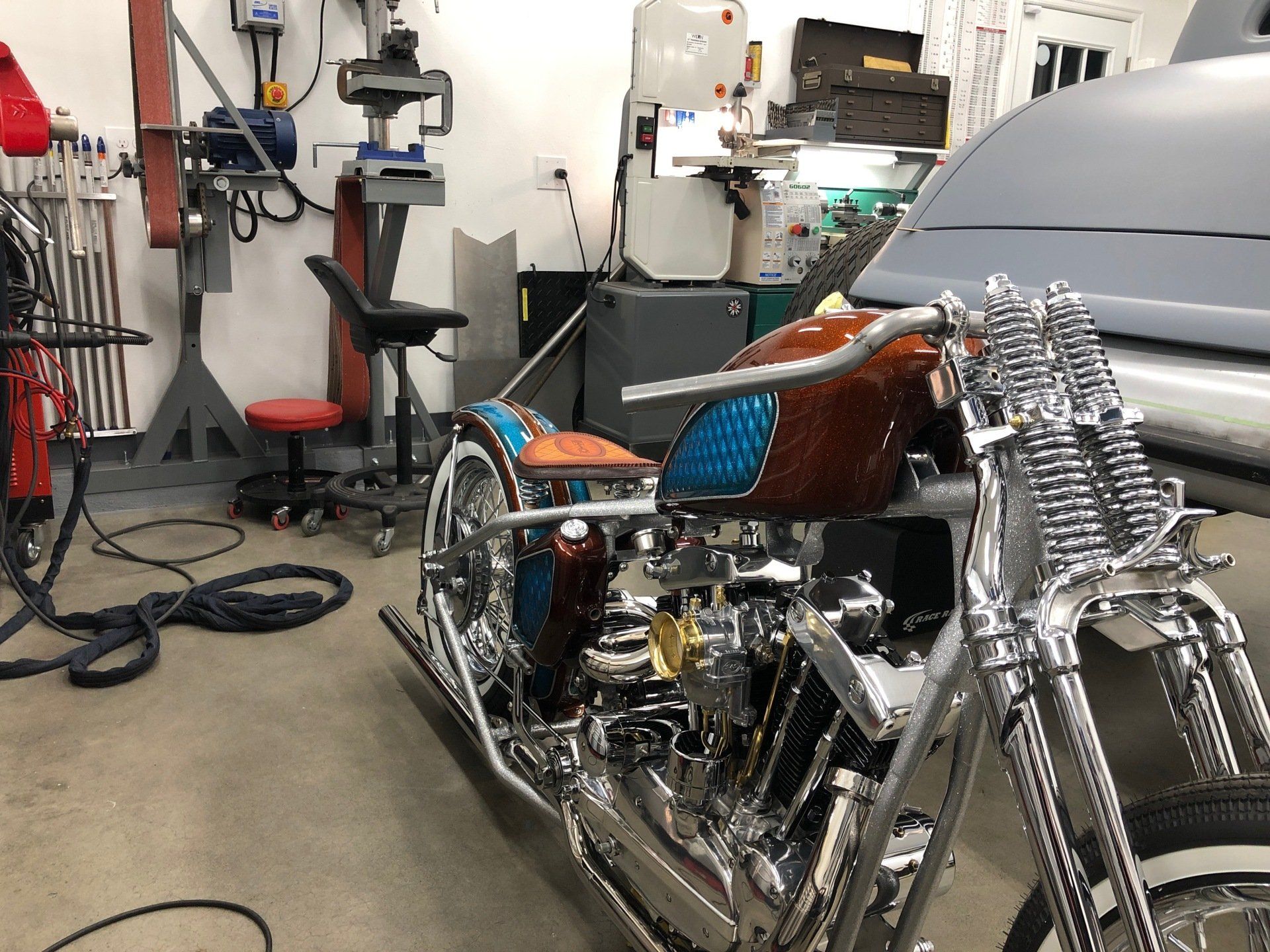 Chrome motorcycle in a workshop garage beside tools and a partially covered car