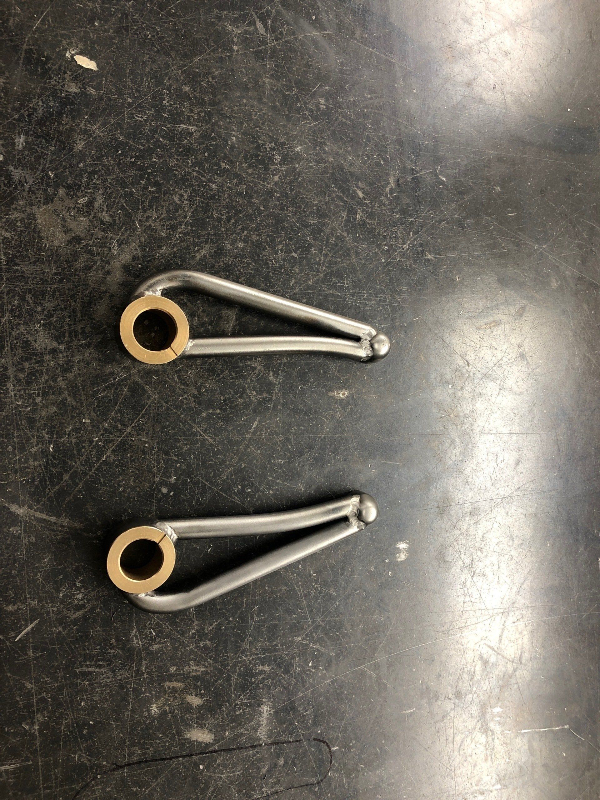 Two small metal safety pins on a dark speckled tabletop, one above the other.
