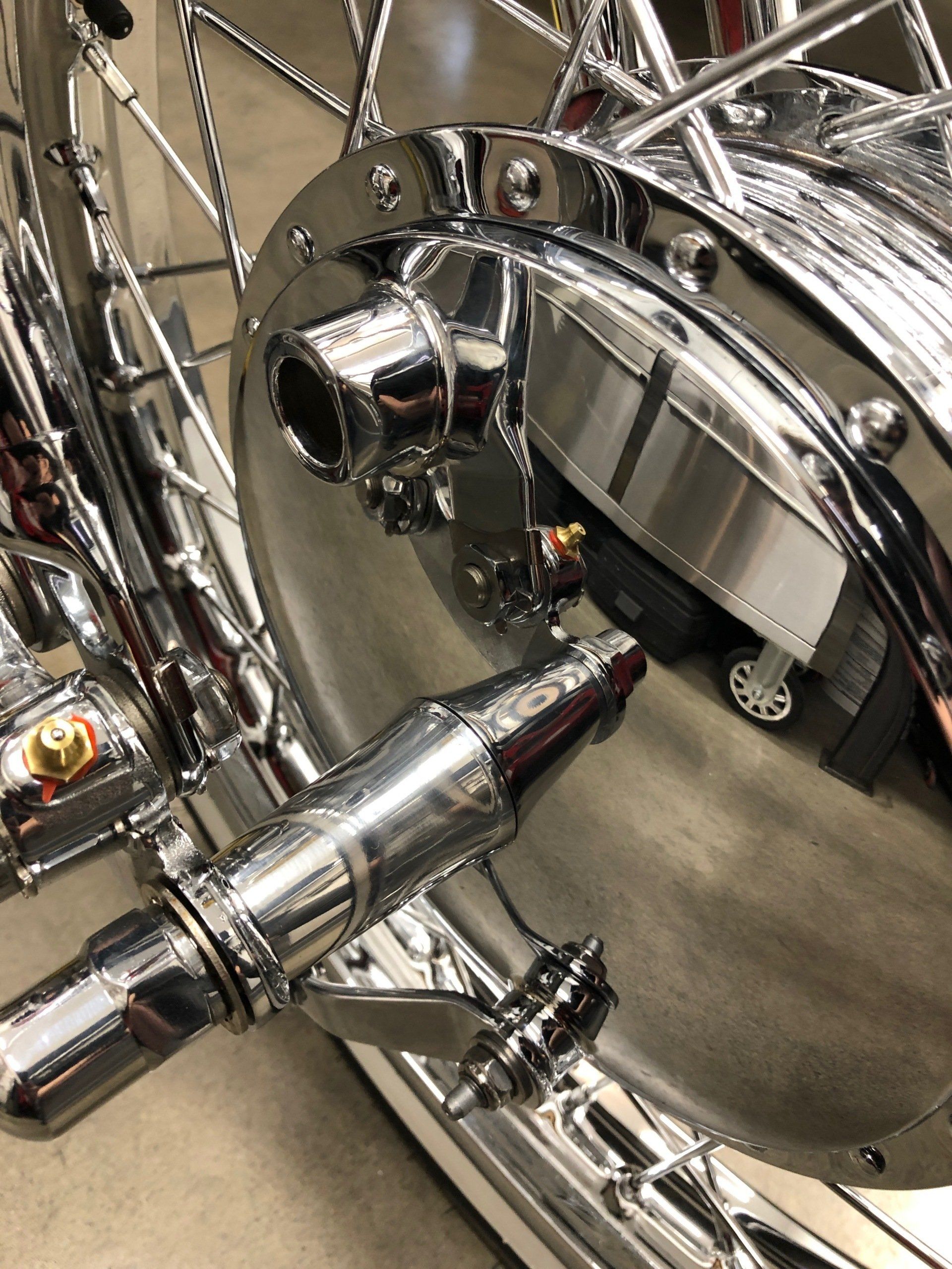Chrome motorcycle wheel hub and spokes with a polished exhaust pipe close-up