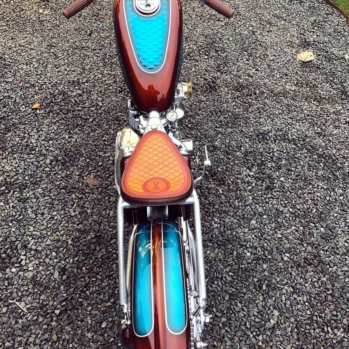 Top-down view of a vintage motorcycle with maroon and turquoise details on gravel.