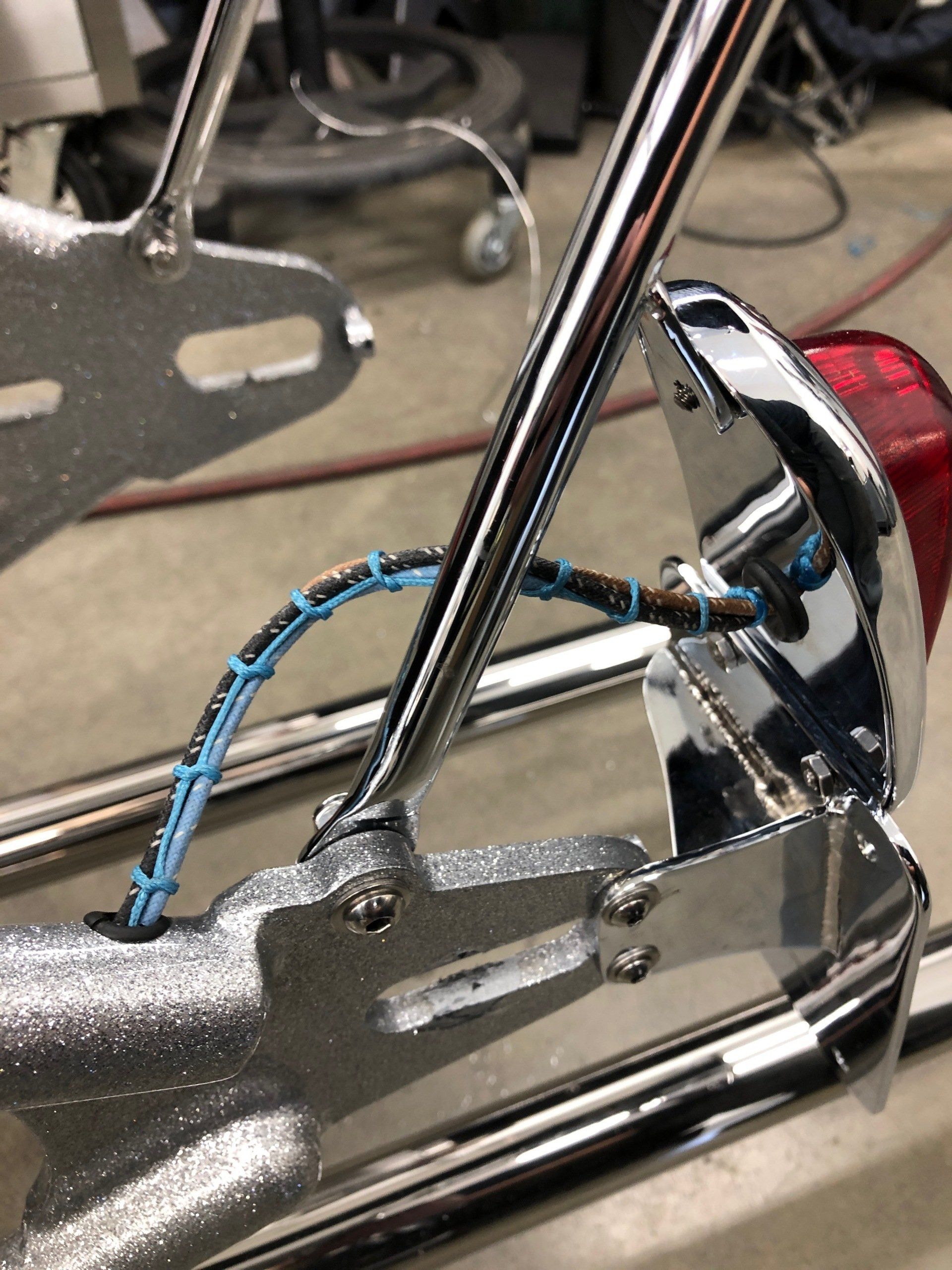Close-up of a chrome bicycle rear frame and red reflector with a blue cable looped around it.