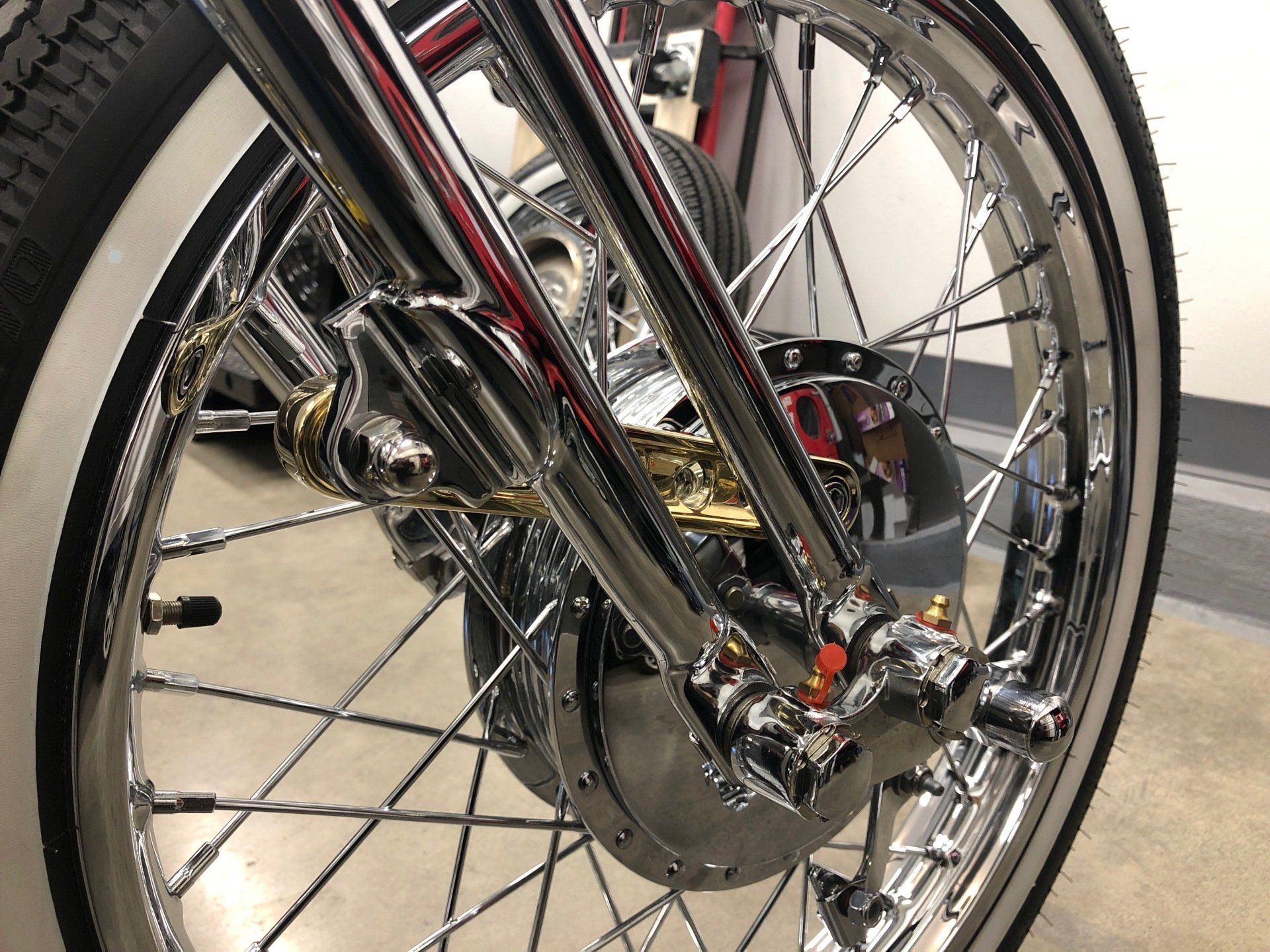 Close-up of a chrome bicycle wheel and frame indoors, showing shiny spokes and mechanical details