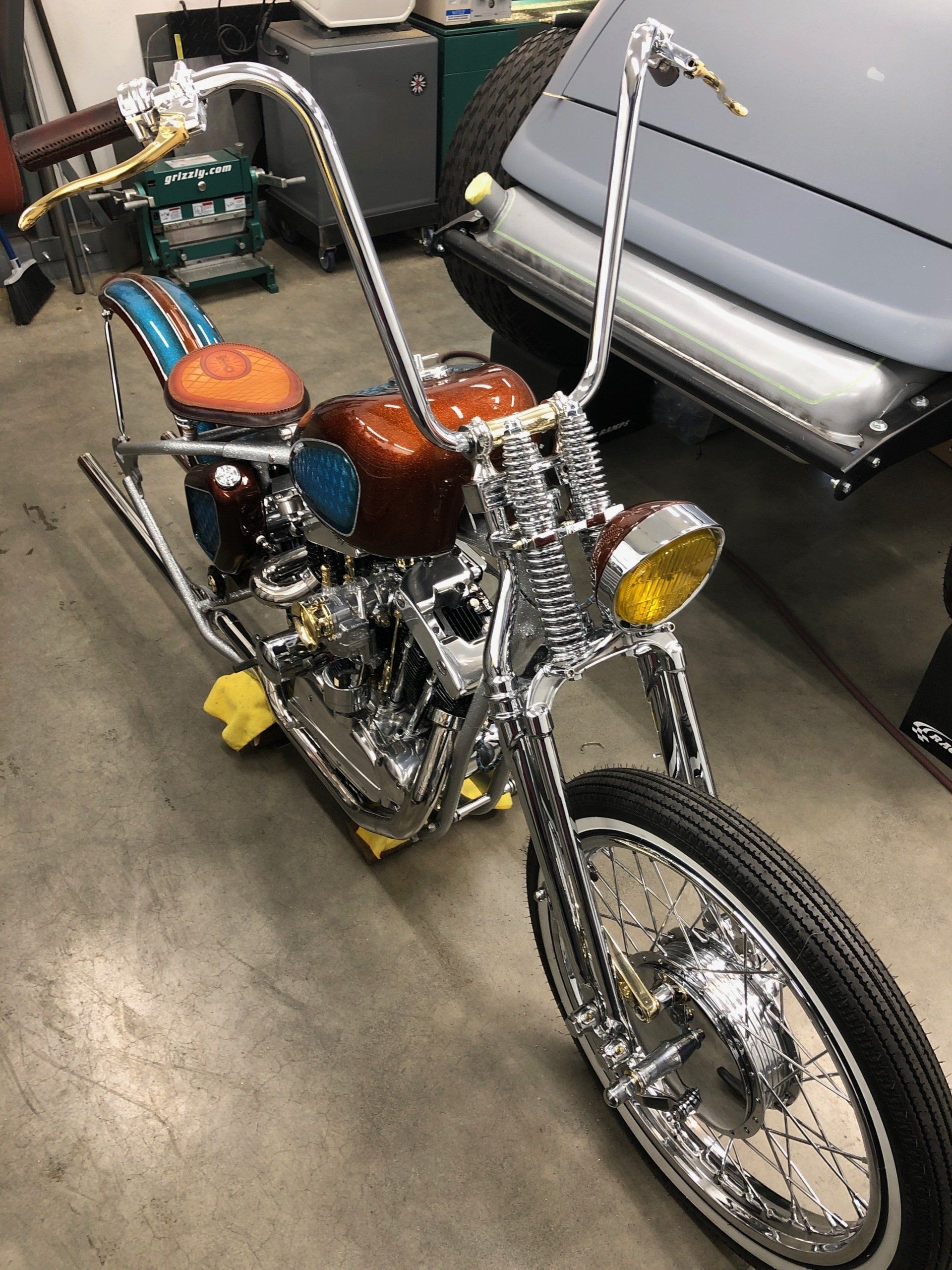 Chrome custom chopper motorcycle with tall handlebars and tan and brown leather seat in a garage