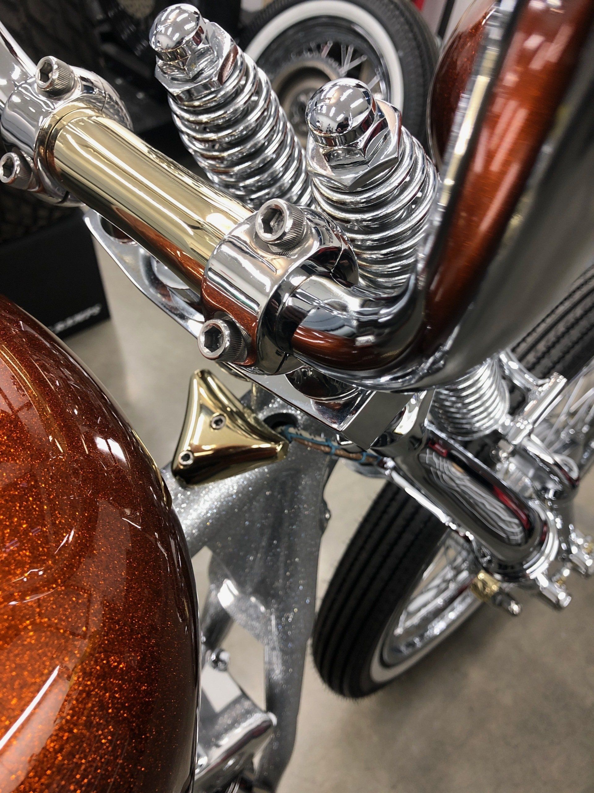 Close-up of a chrome motorcycle engine and spring suspension beside a brown fuel tank.
