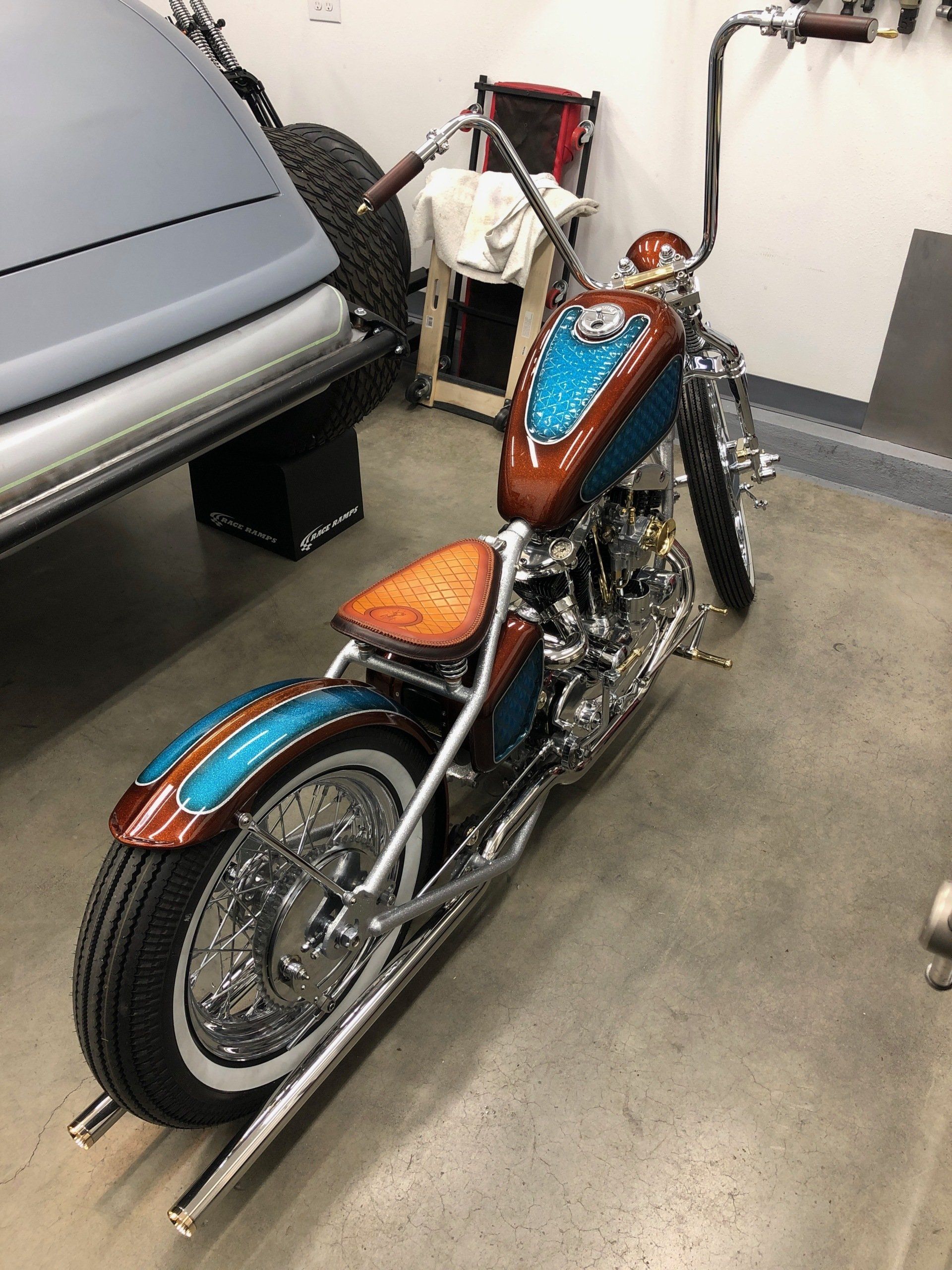 Custom blue-and-copper motorcycle parked indoors next to a gray vehicle
