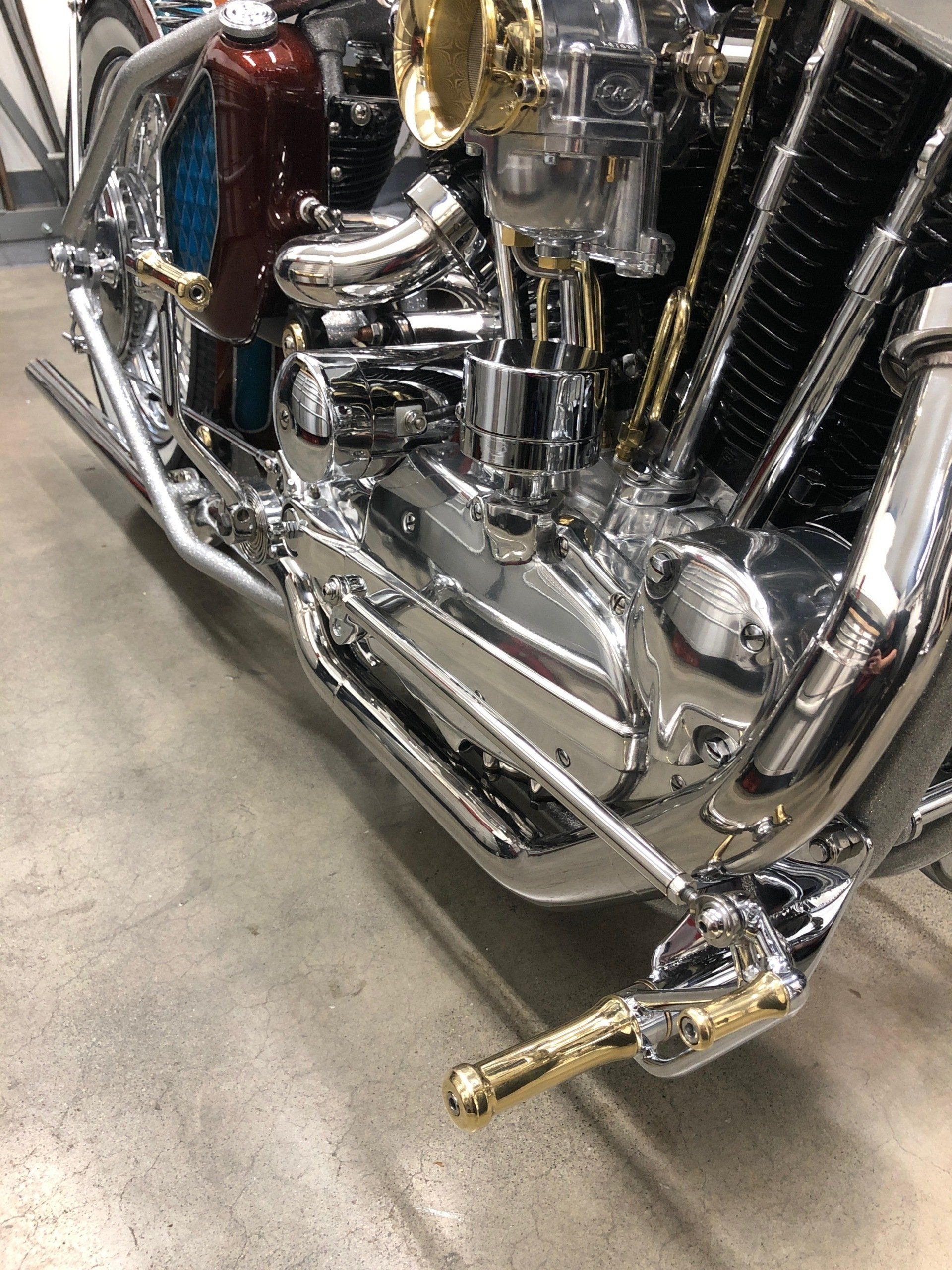 Chrome motorcycle engine and exhaust with a gold foot peg on a concrete floor