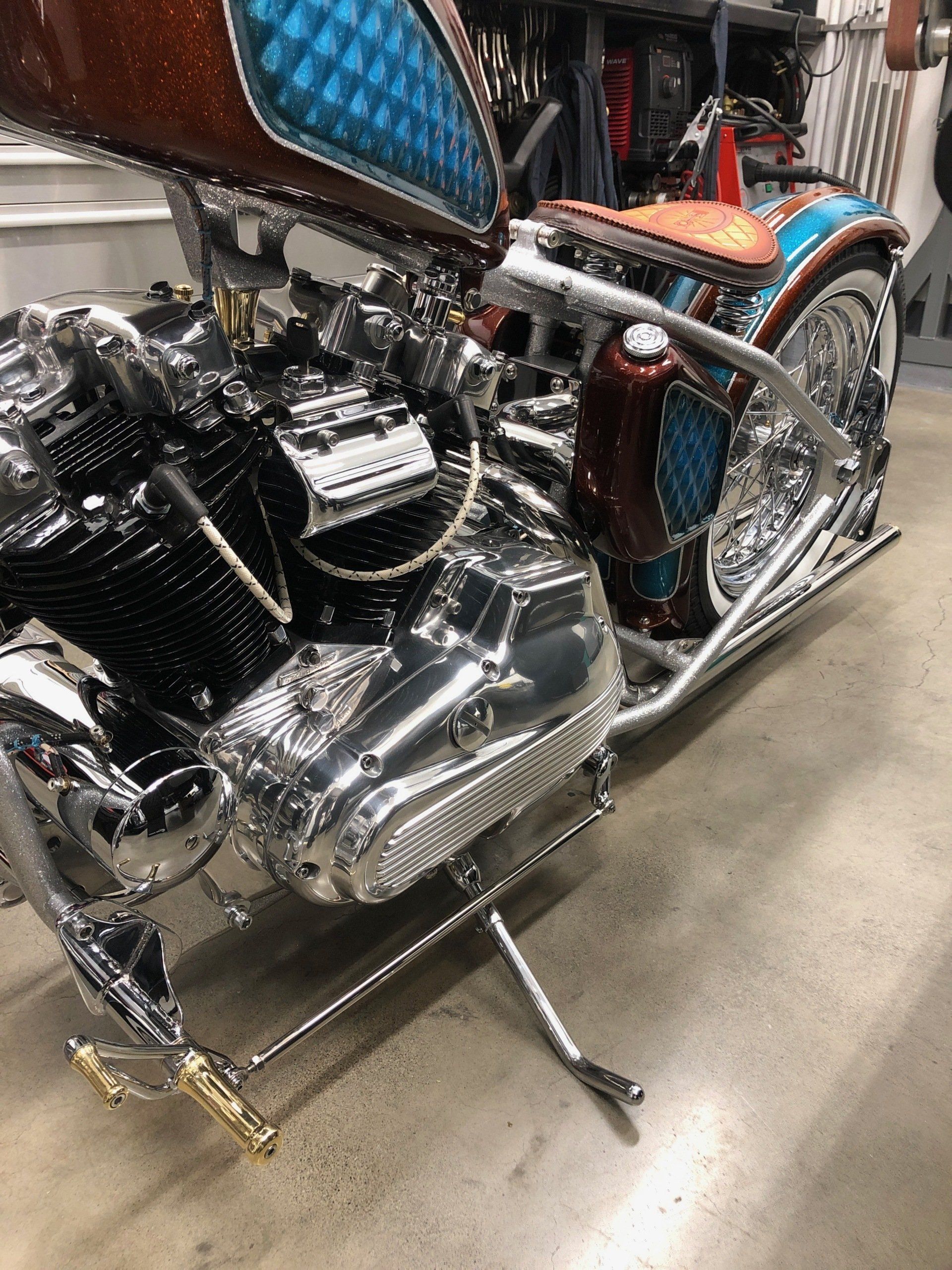 Chrome custom motorcycle with a V-twin engine and blue-orange accents on display indoors