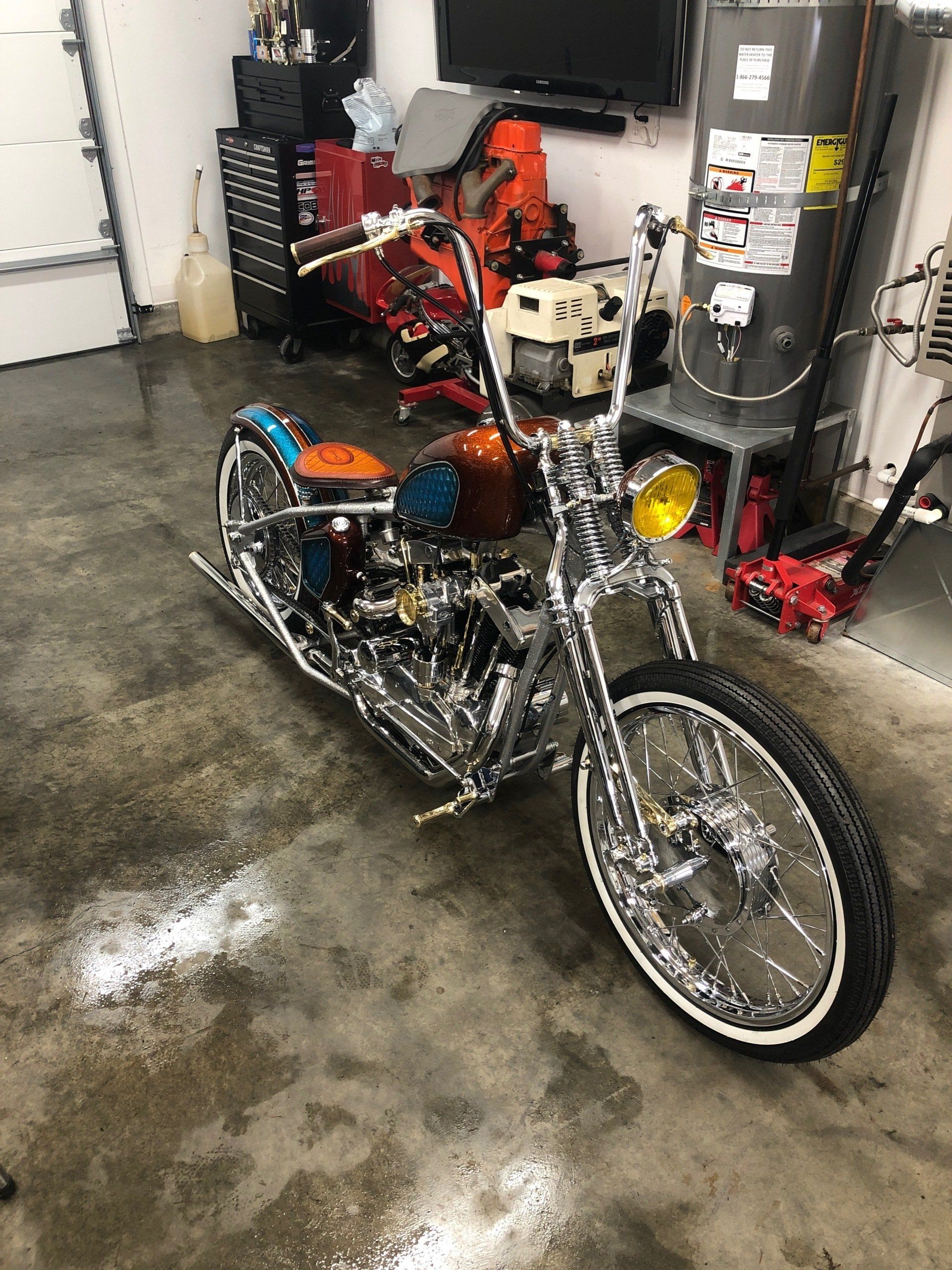Chrome chopper-style motorcycle in a garage with red and black accents, parked on a concrete floor