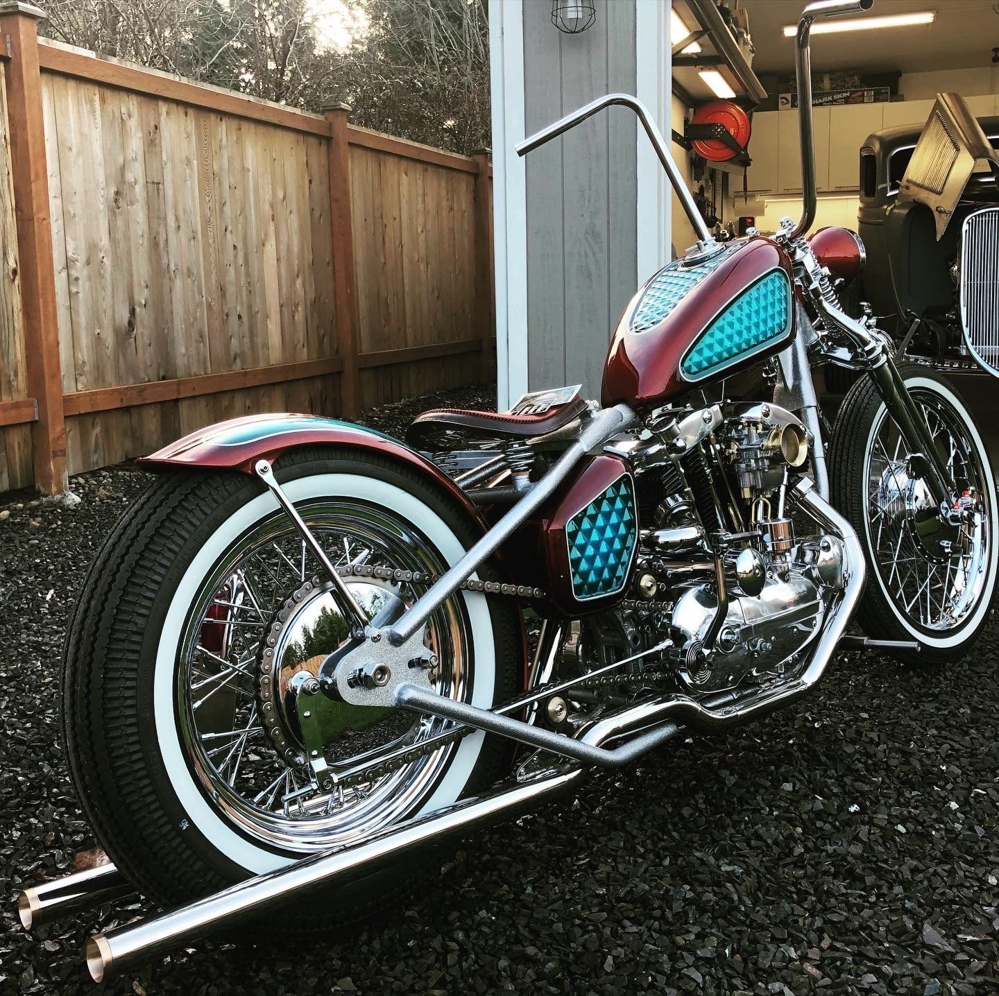 Custom chrome motorcycle with pink and blue accents parked beside a wooden fence.