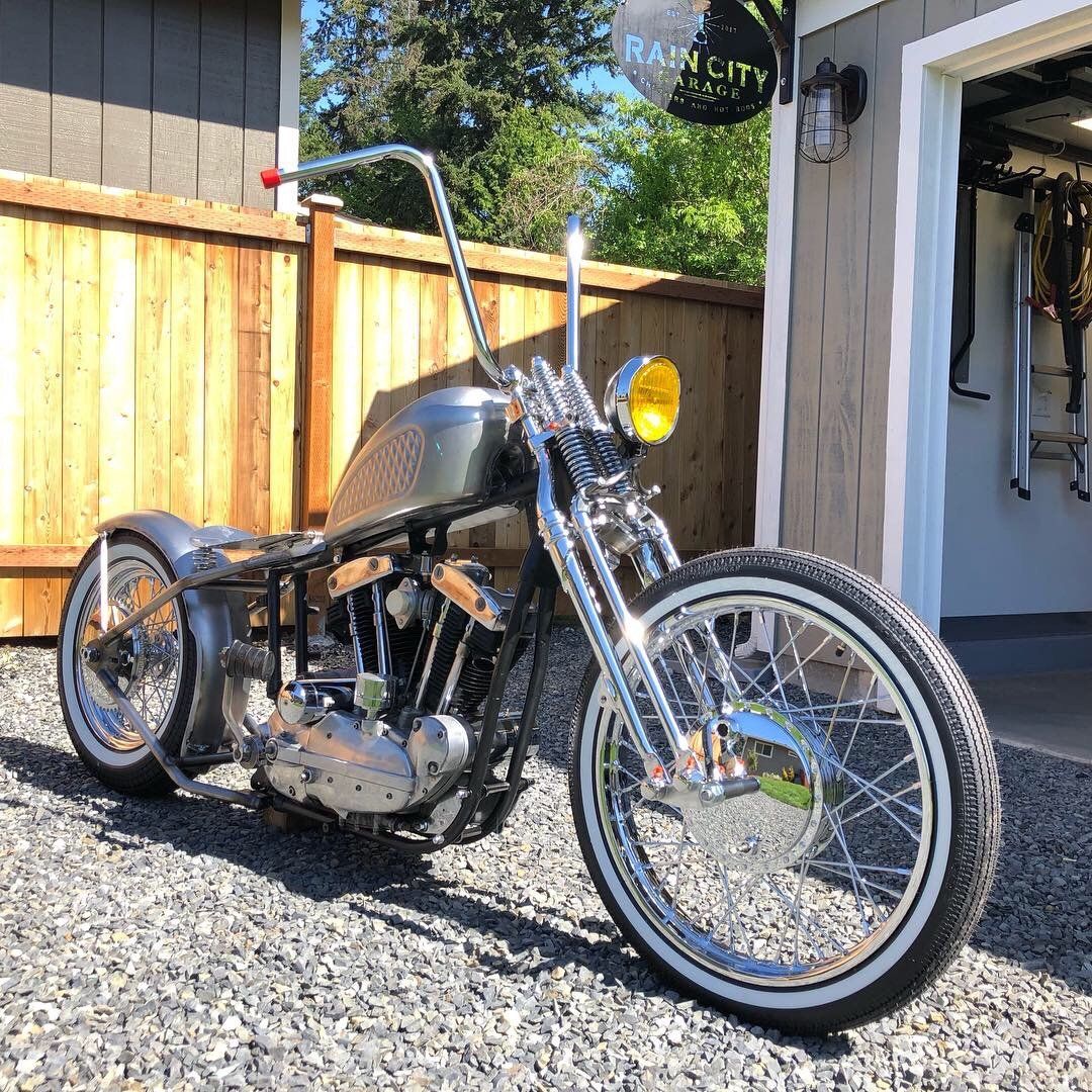 Custom black chopper motorcycle parked on gravel beside a wooden fence in sunlight