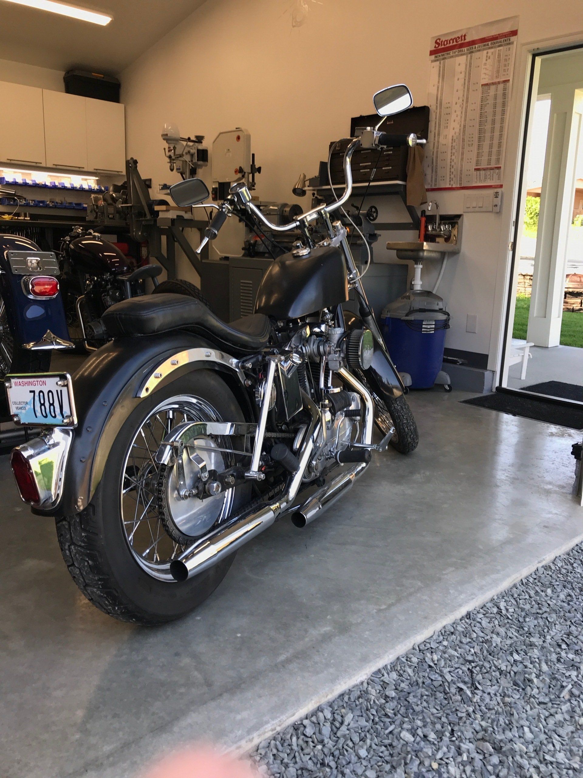 Black motorcycle parked in a garage on a concrete floor, with tools and shelves in the background.