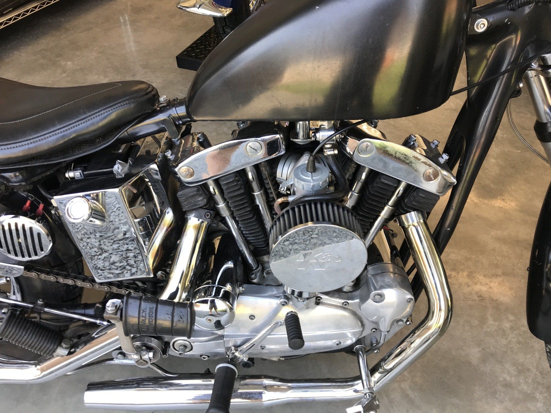 Black motorcycle engine and chrome exhaust beneath a black seat and fuel tank.