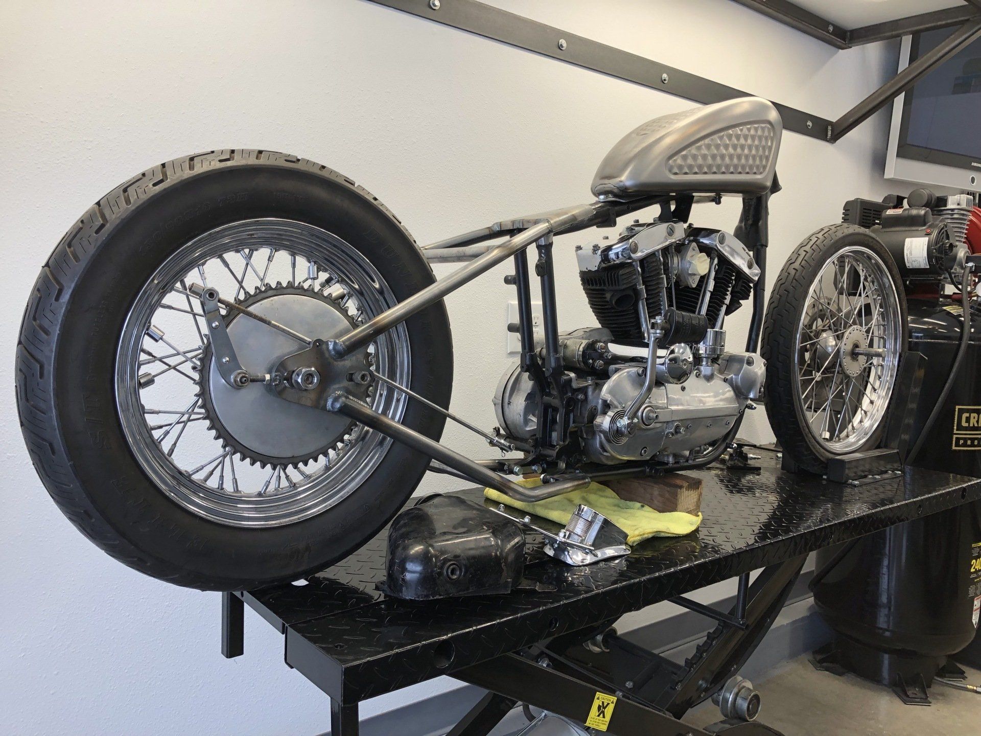 Custom low-profile motorcycle on a display stand in a garage, with large spoked wheels and exposed engine.