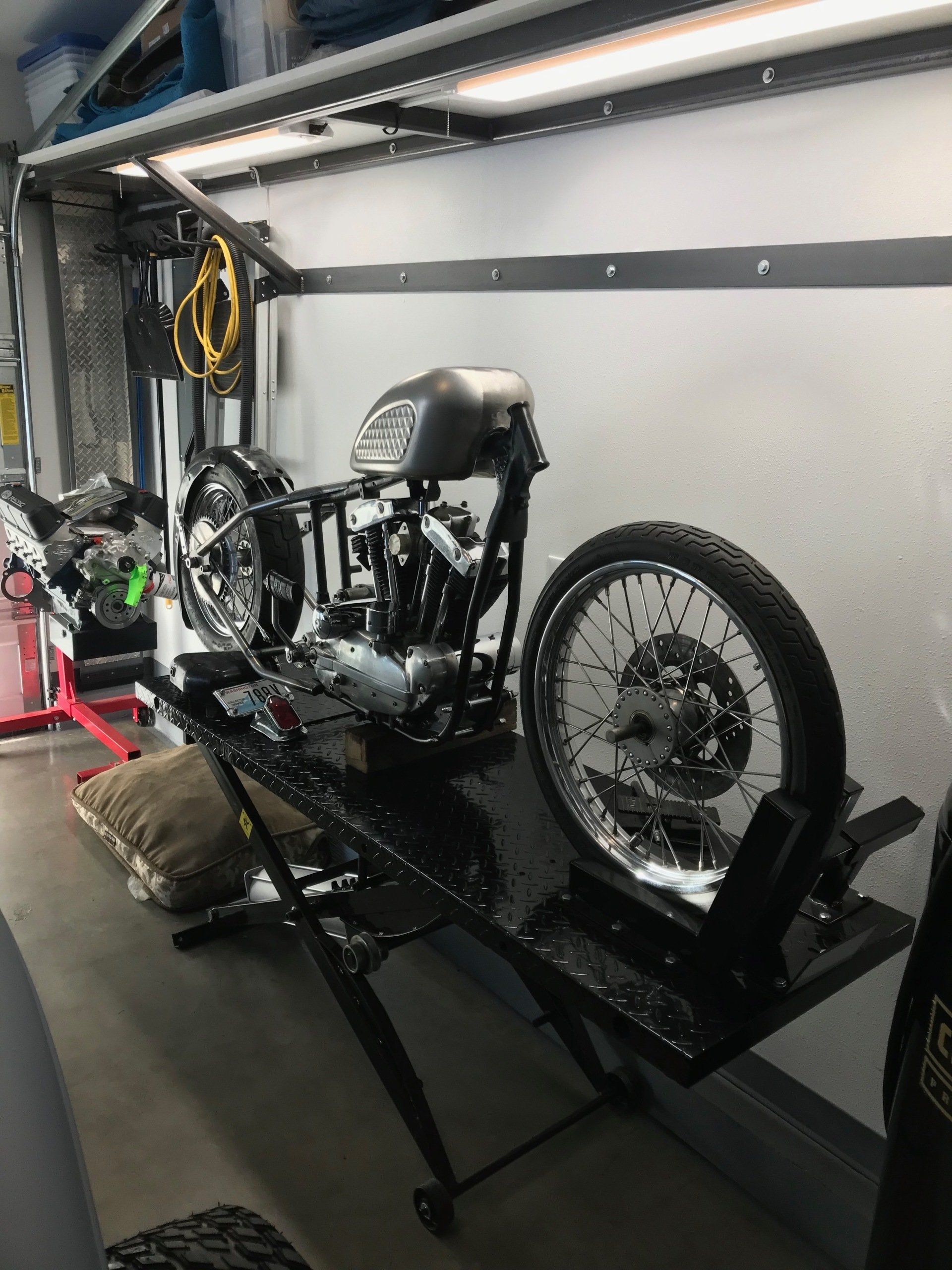 Motorcycle on a lift in a garage, with front wheel removed and parts exposed.