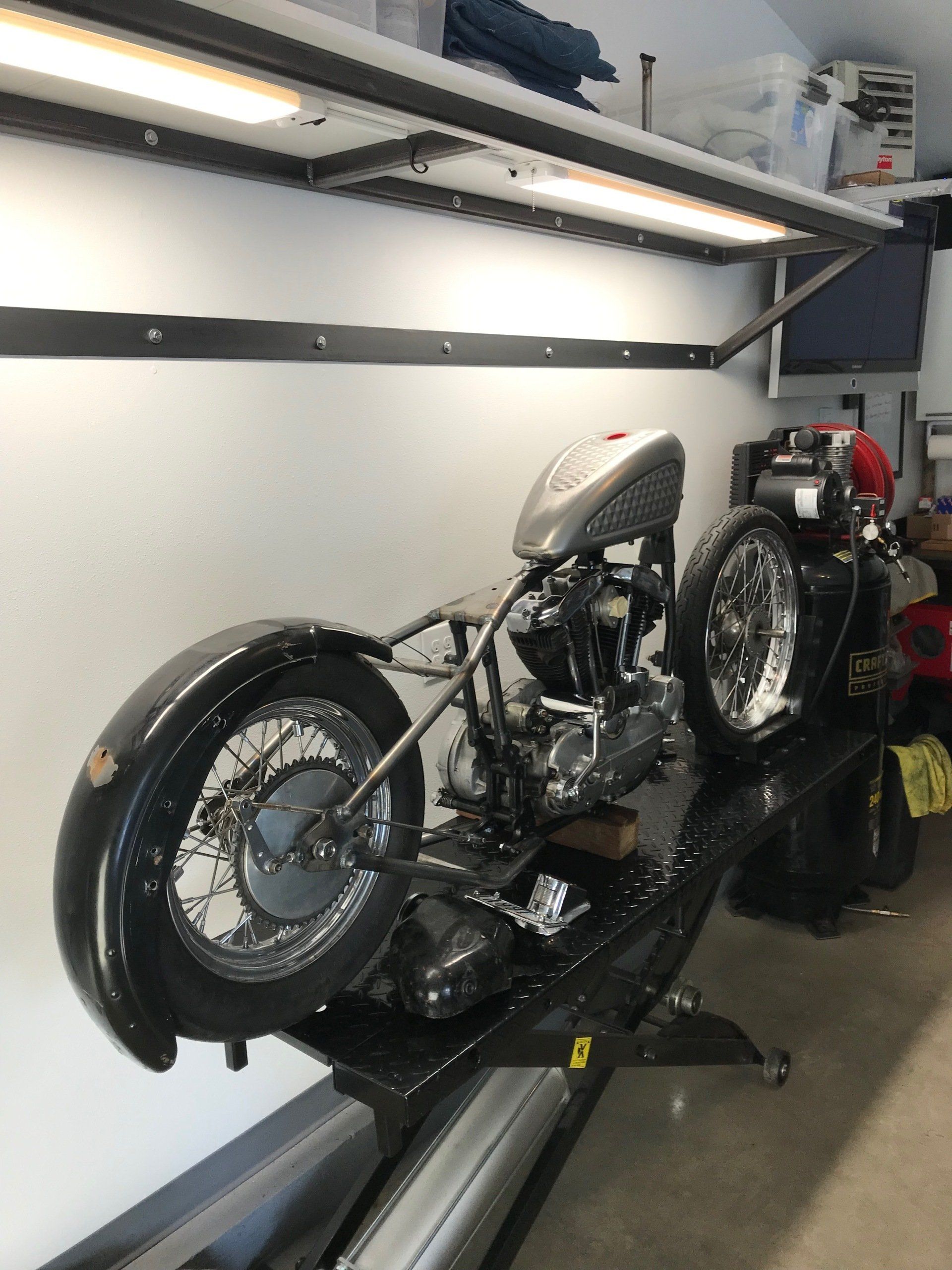 Custom motorcycle on a trailer inside a garage, with a white fuel tank and chrome engine.