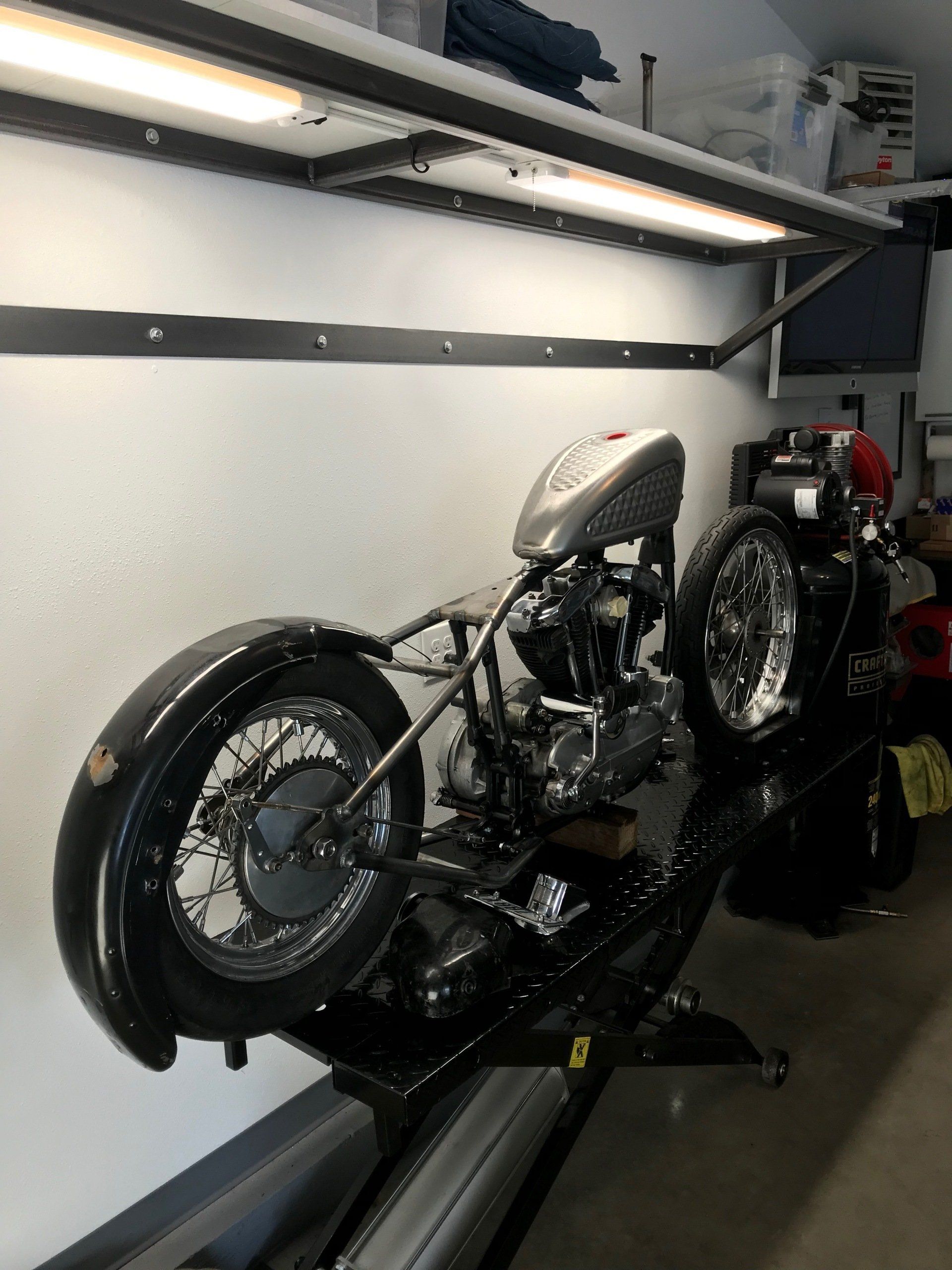 Custom motorcycle on a trailer inside a garage, with chrome engine and white fuel tank.