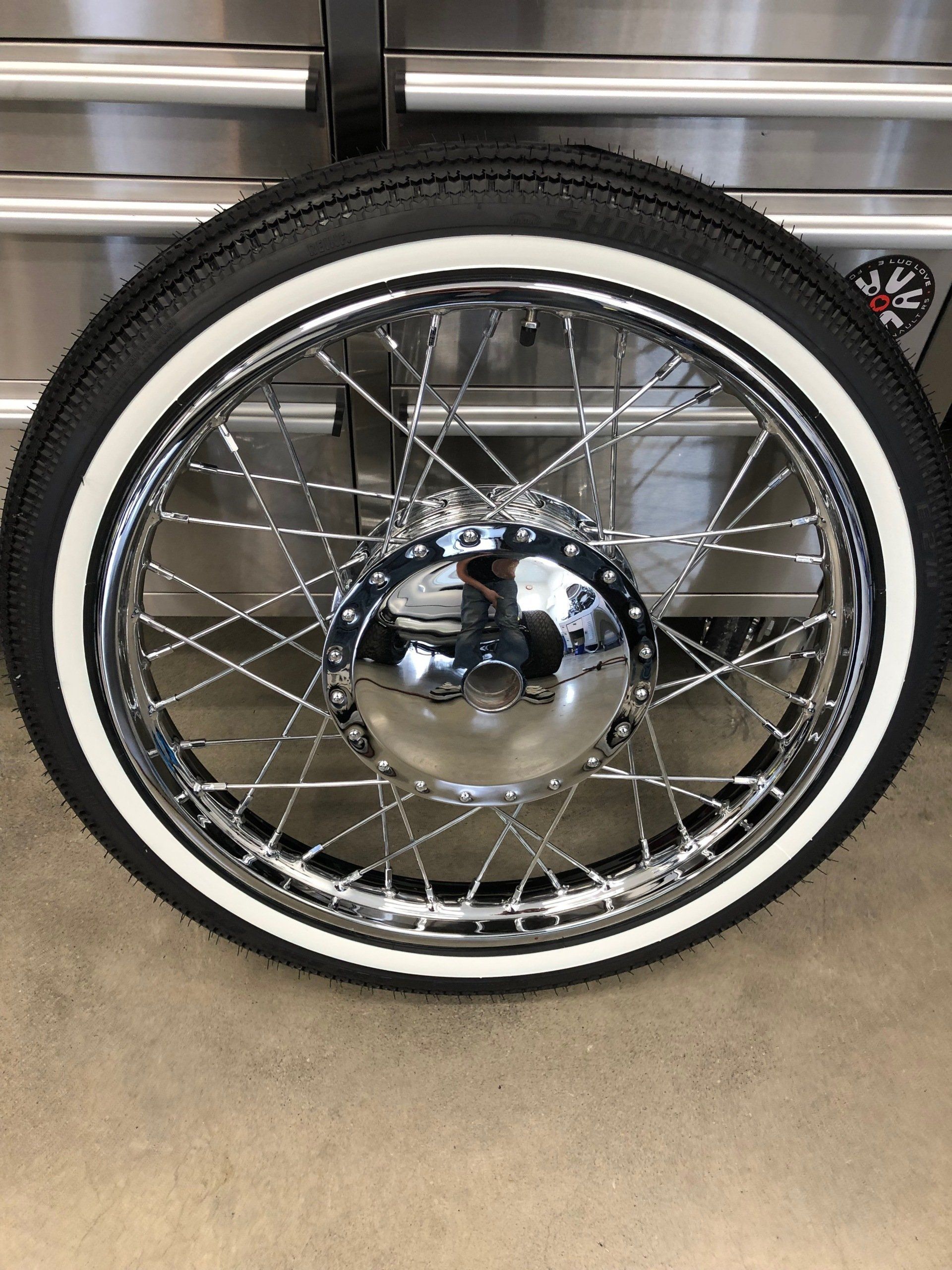 Chrome-spoked bicycle wheel with whitewall tire against a metal garage door