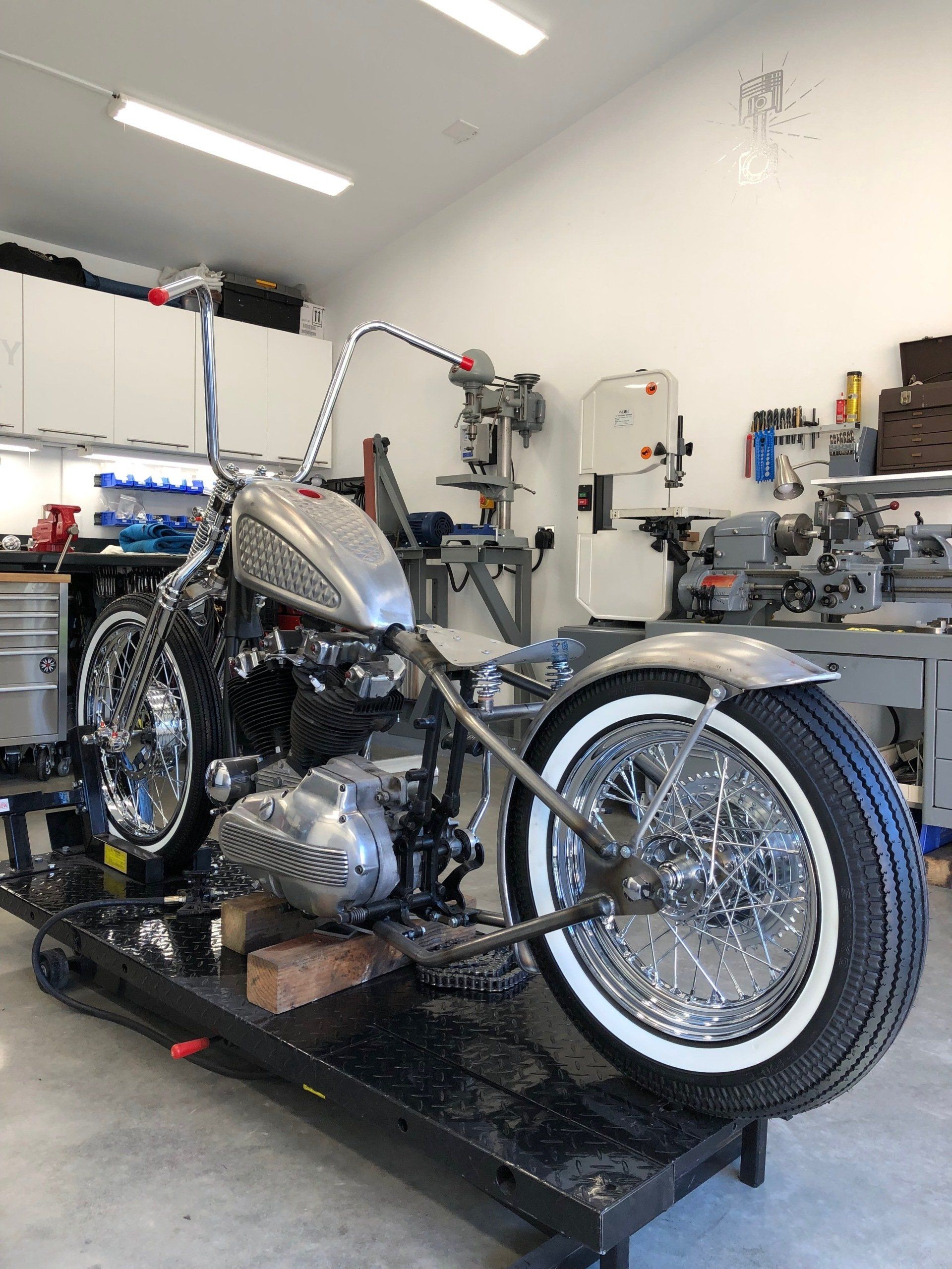 Custom black motorcycle on a workshop lift in a bright garage, with chrome details and whitewall front tire