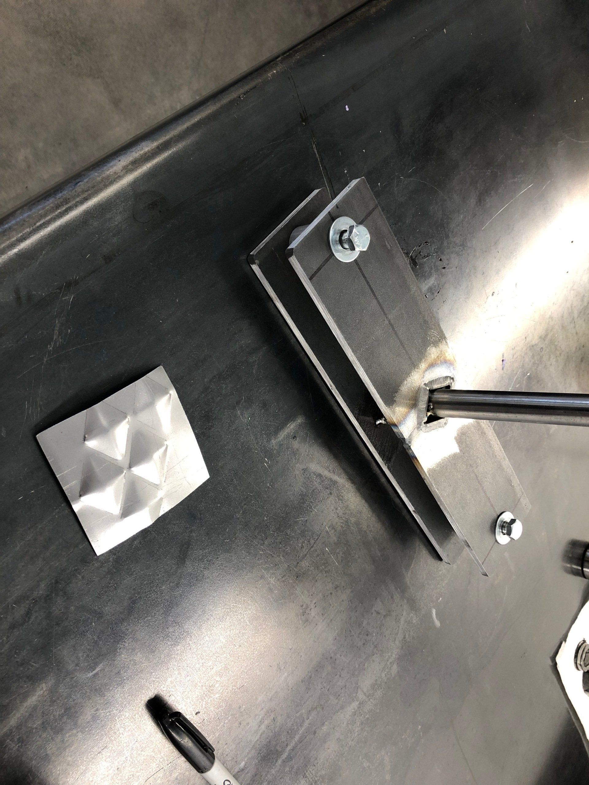 Close-up of a black metal panel with a square button and a screwdriver near a mounted bracket.