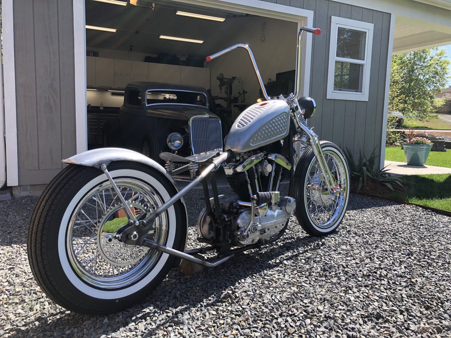Custom motorcycle parked in front of an open garage, with chrome details and whitewall tires.