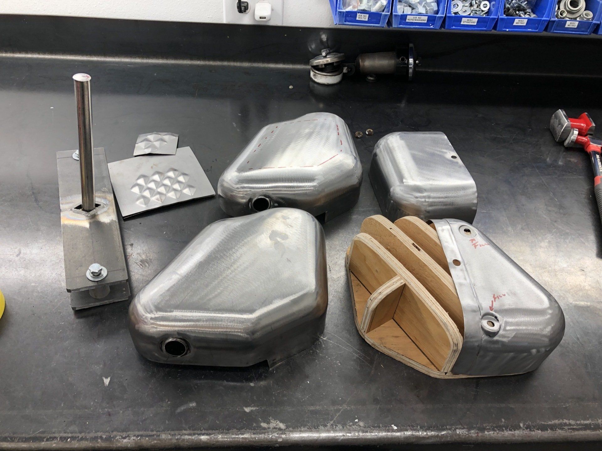 Assorted metal parts and tools on a workbench, including gray housings and a wooden-handled component.