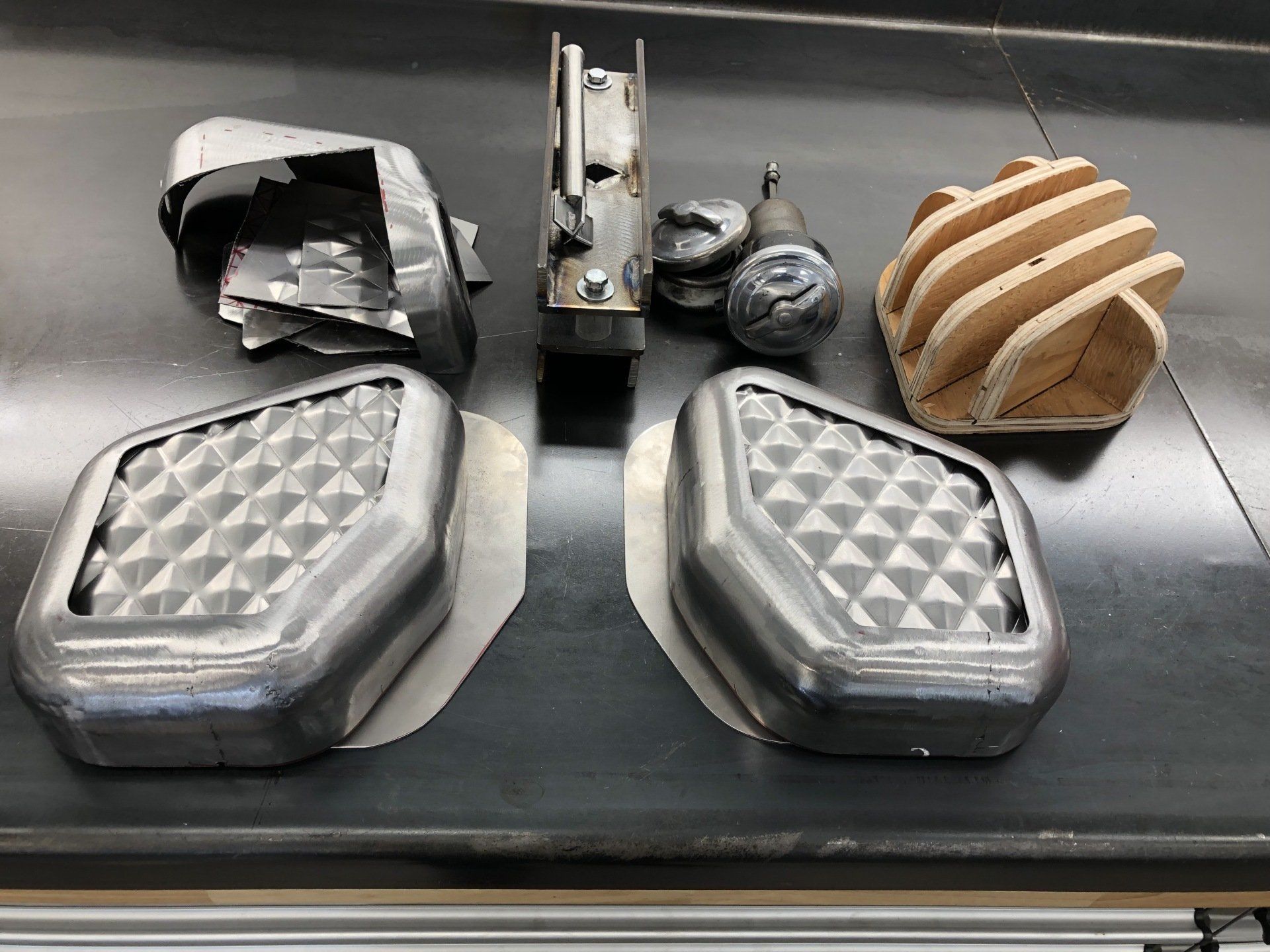 Two open aluminum food containers with lids, small cups, and sliced bread on a black table.