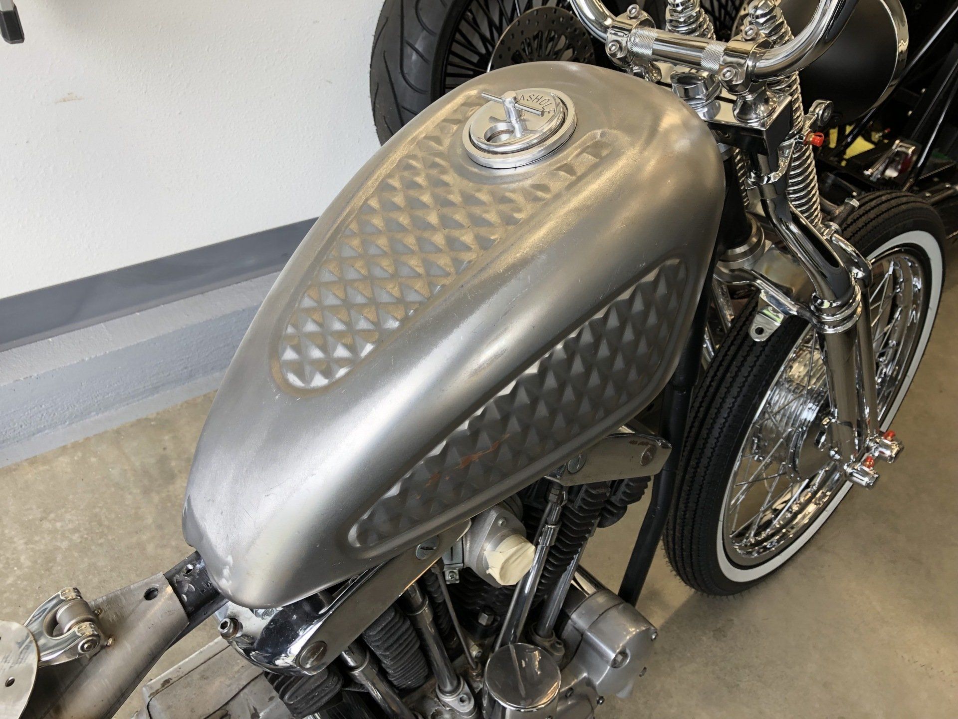 Custom silver motorcycle with diamond-pattern fuel tank in a garage