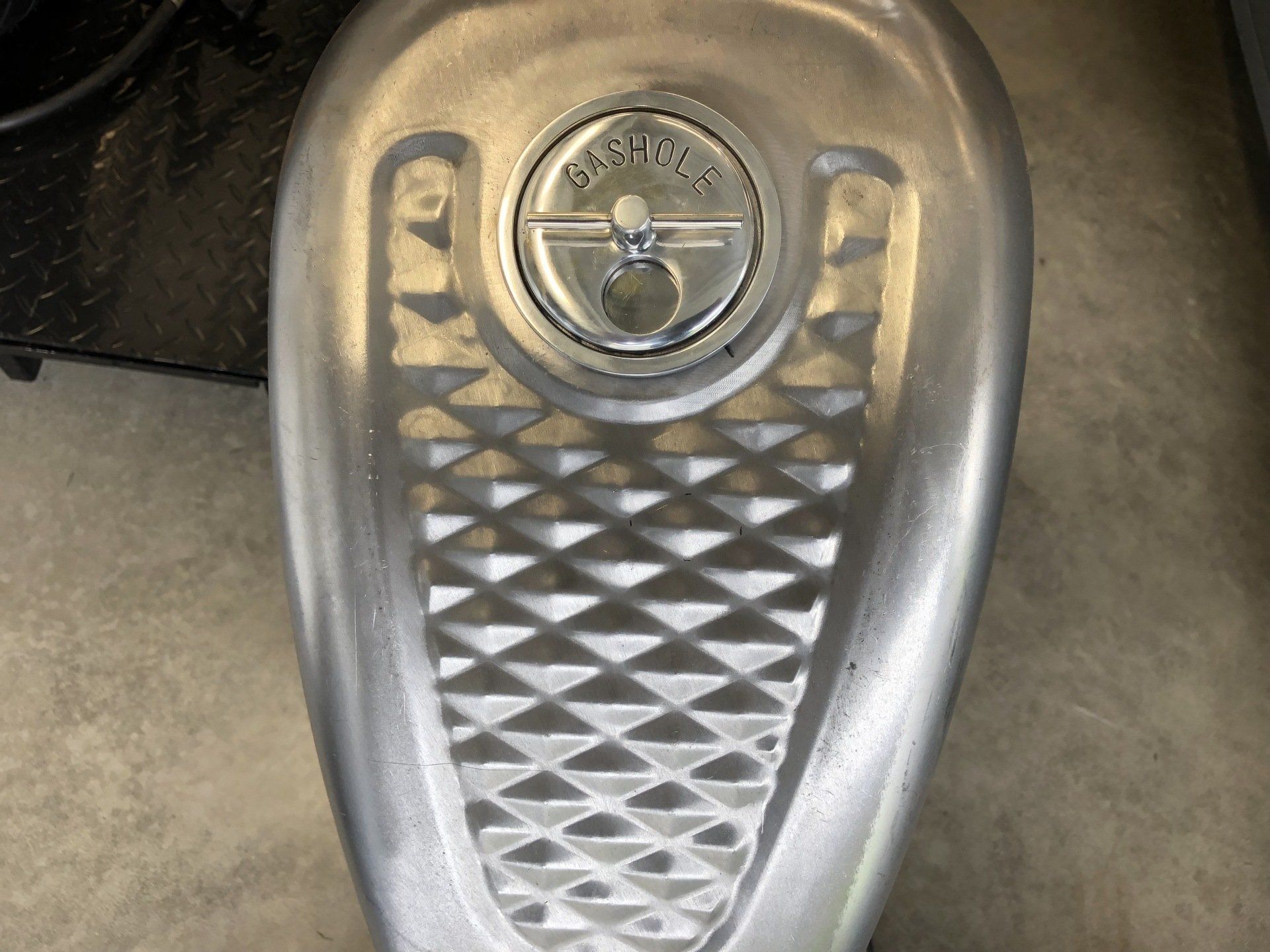 Close-up of a silver vintage car hood ornament with a diamond-patterned grille and circular emblem