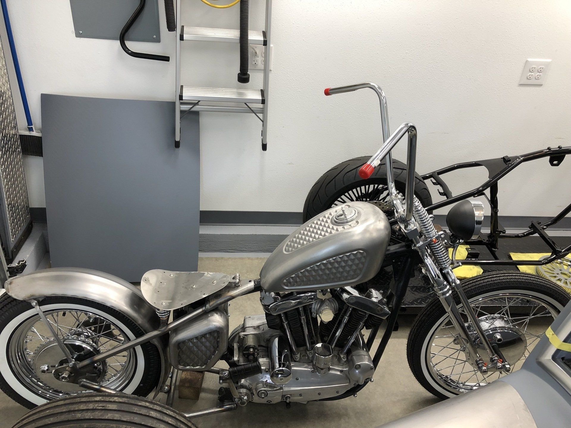 Custom chopper motorcycle in a garage, with a silver fuel tank and chrome frame.