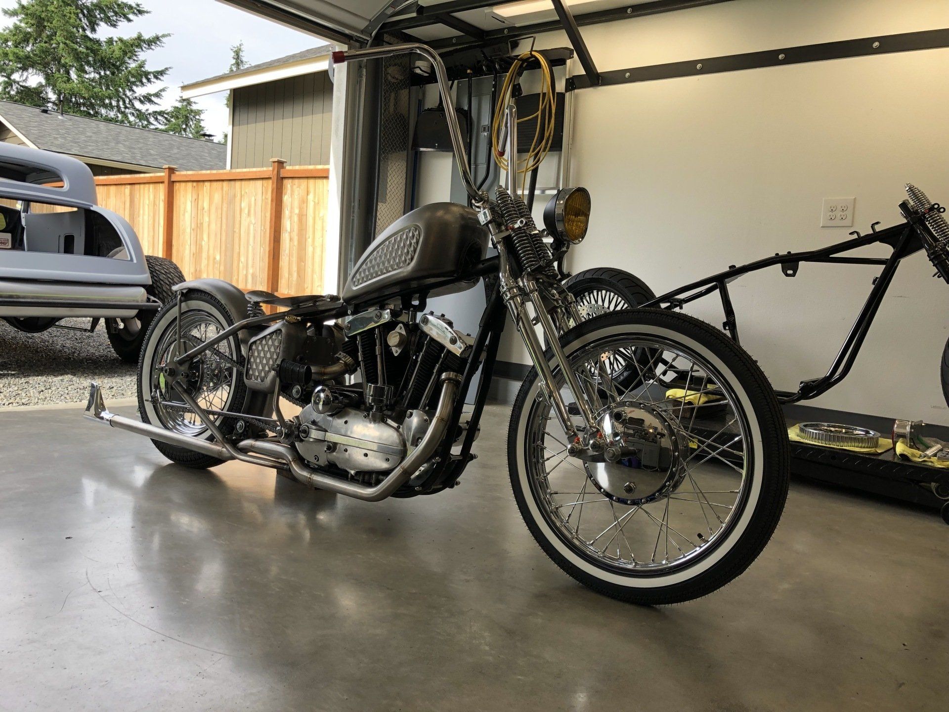 Custom black motorcycle in a garage, with a bare frame bike behind it.