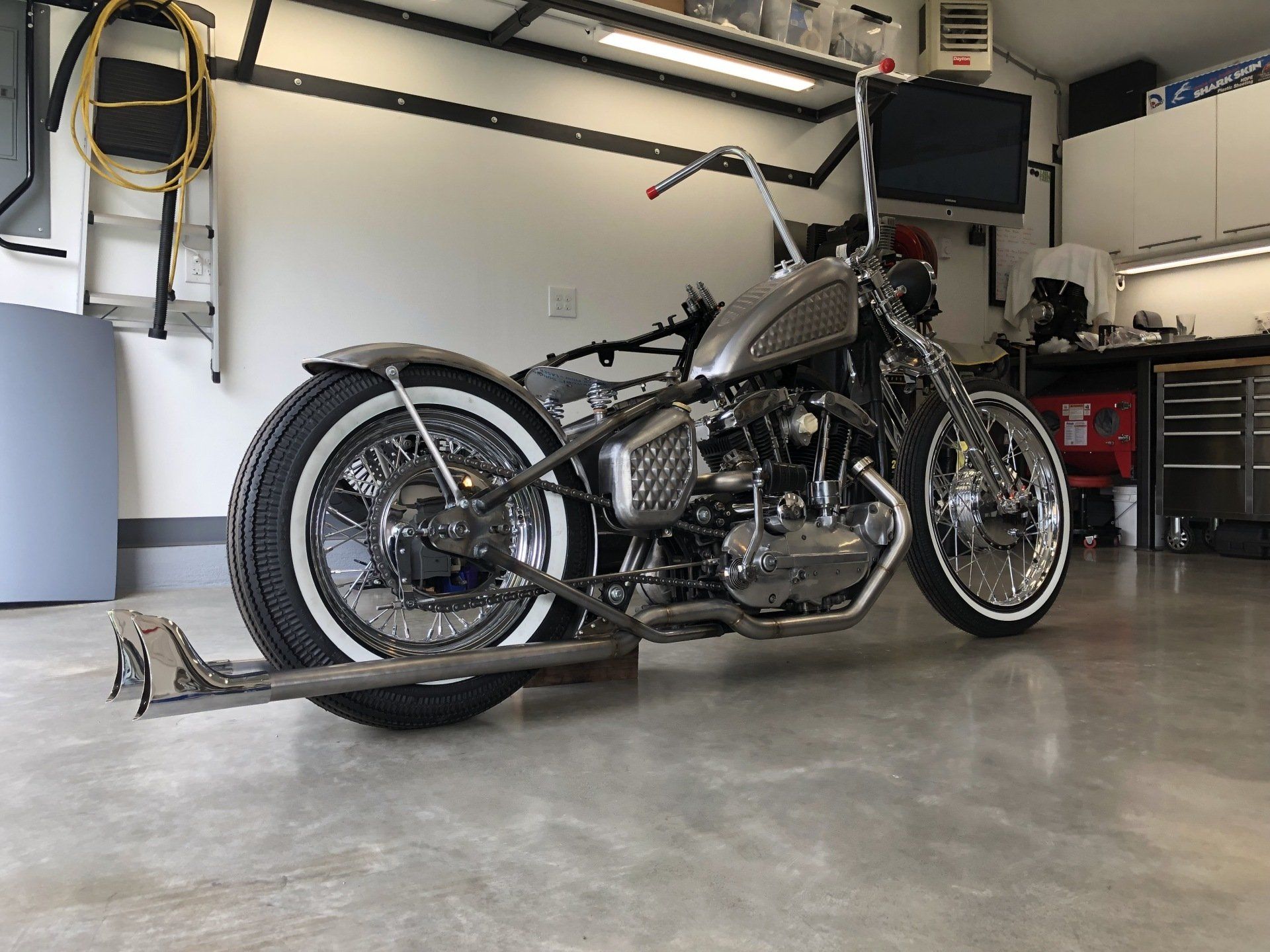 Custom black chopper motorcycle in a garage with a rear wheel ramp.