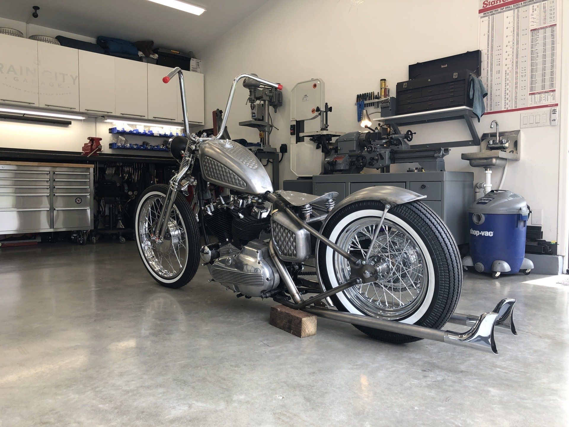Black custom motorcycle in a garage, parked on a stand with tools and equipment around it.