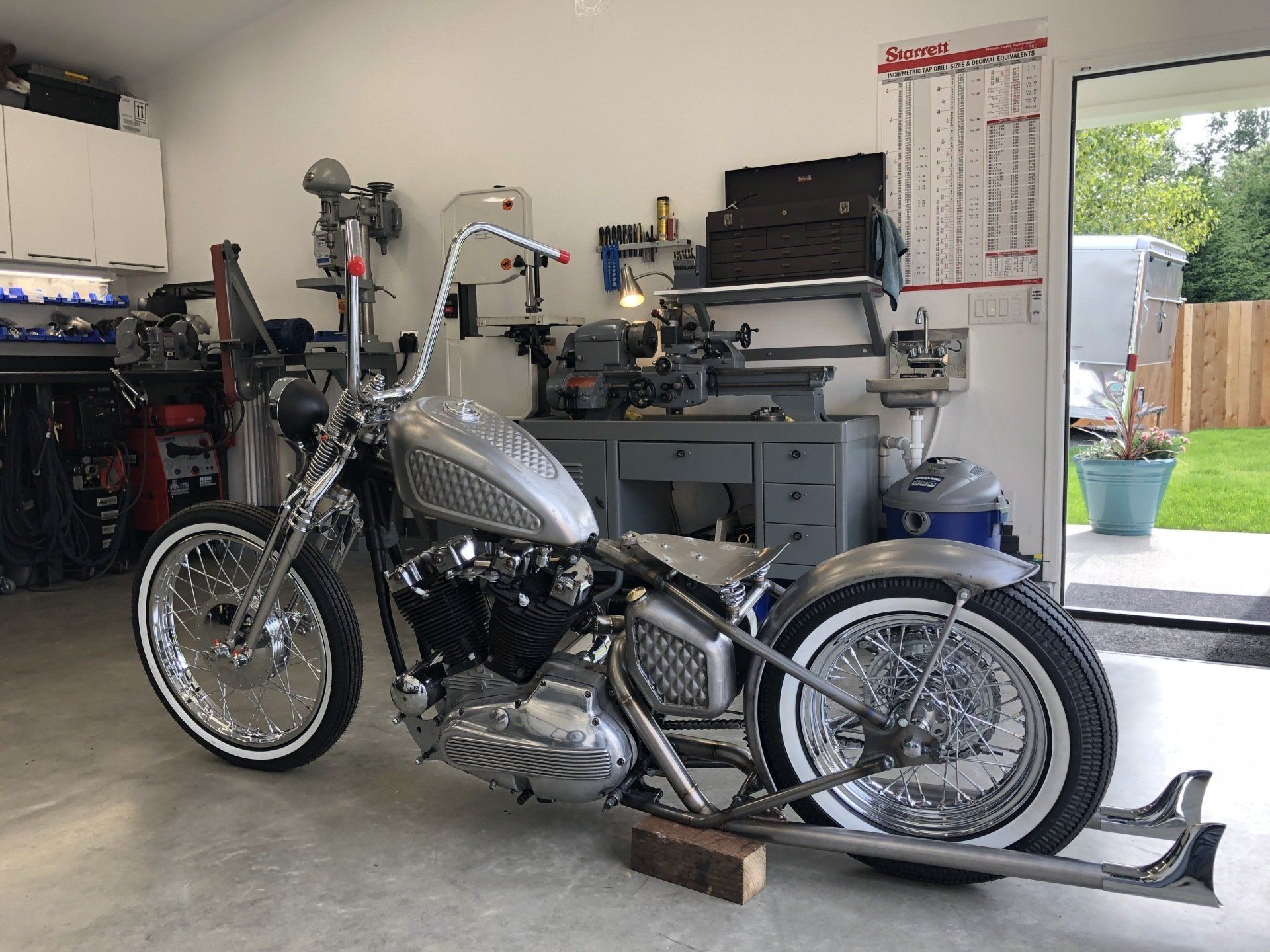 Custom chopper motorcycle parked in a garage, with tools and equipment in the background.