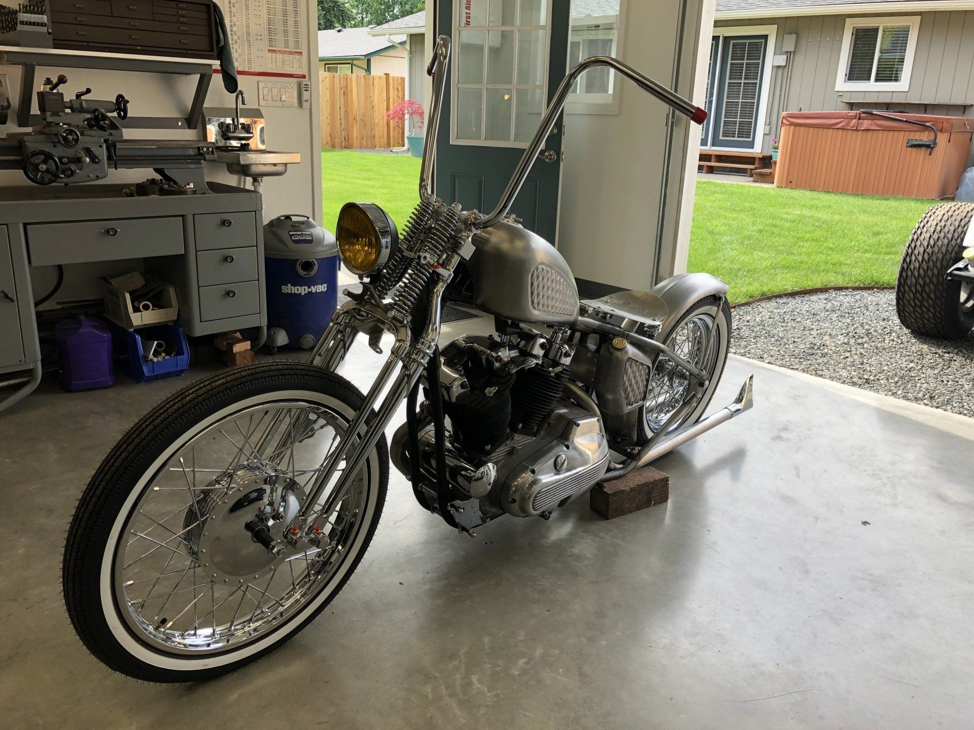 Custom chopper motorcycle in a garage, chrome and black, parked on a concrete floor with yard visible outside