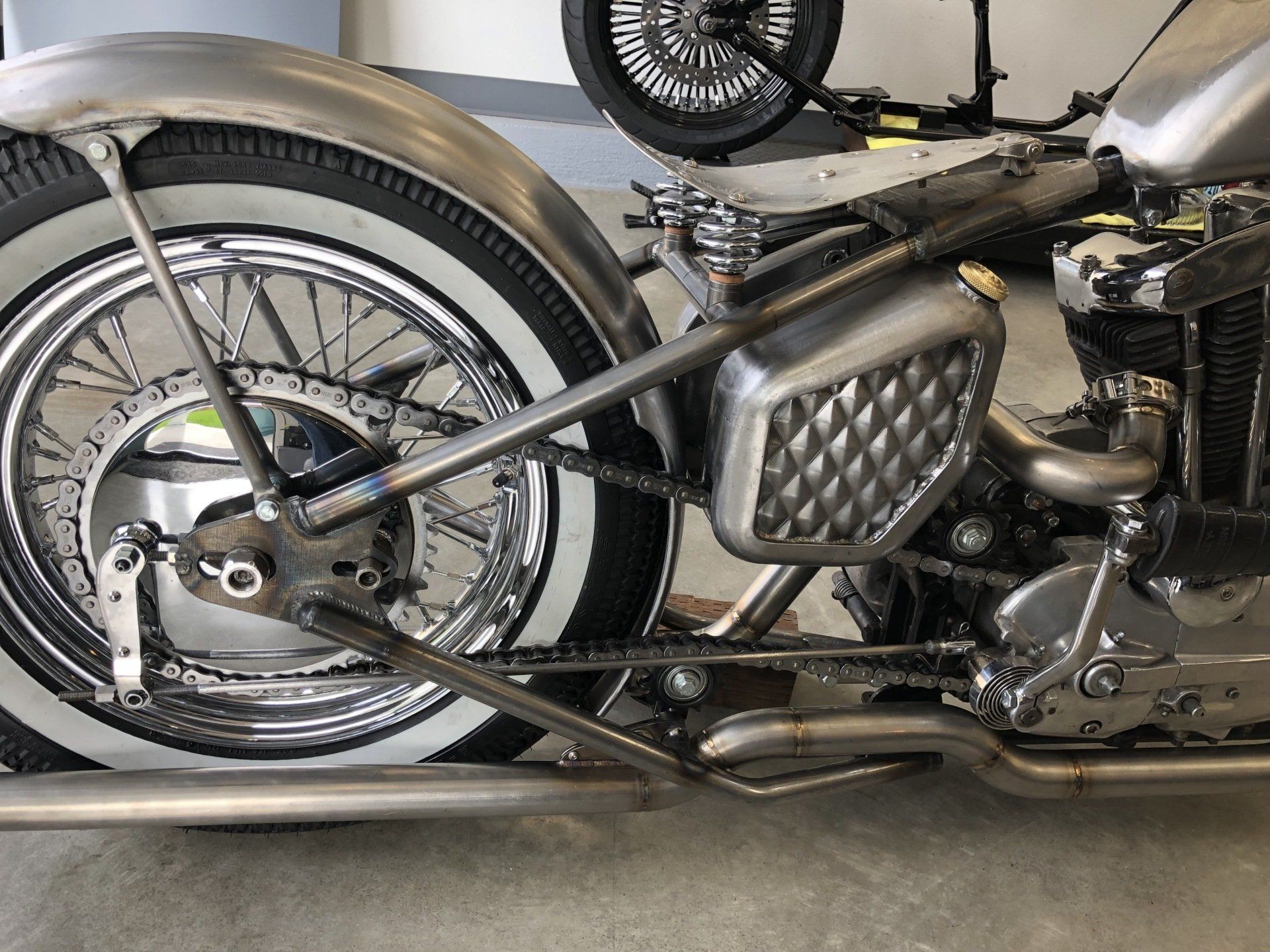 Custom motorcycle frame and chrome rear wheel in a workshop, shown in close-up.