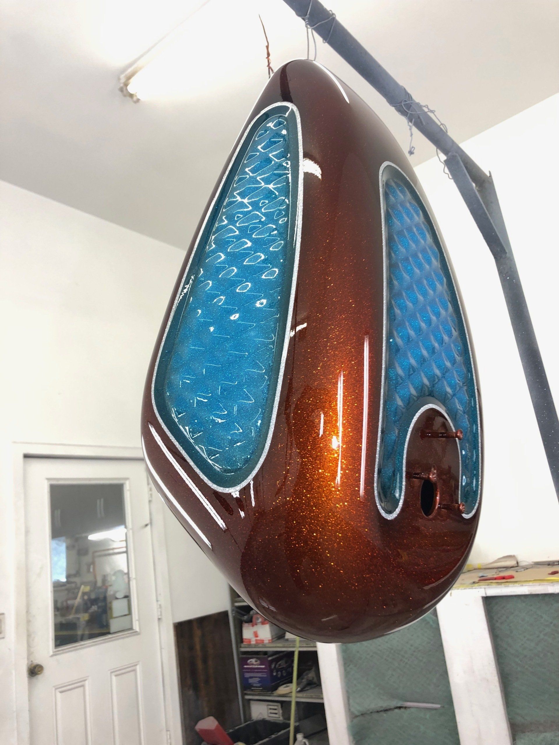 Brown and blue hanging abstract sculpture indoors with glossy, teardrop-shaped panels