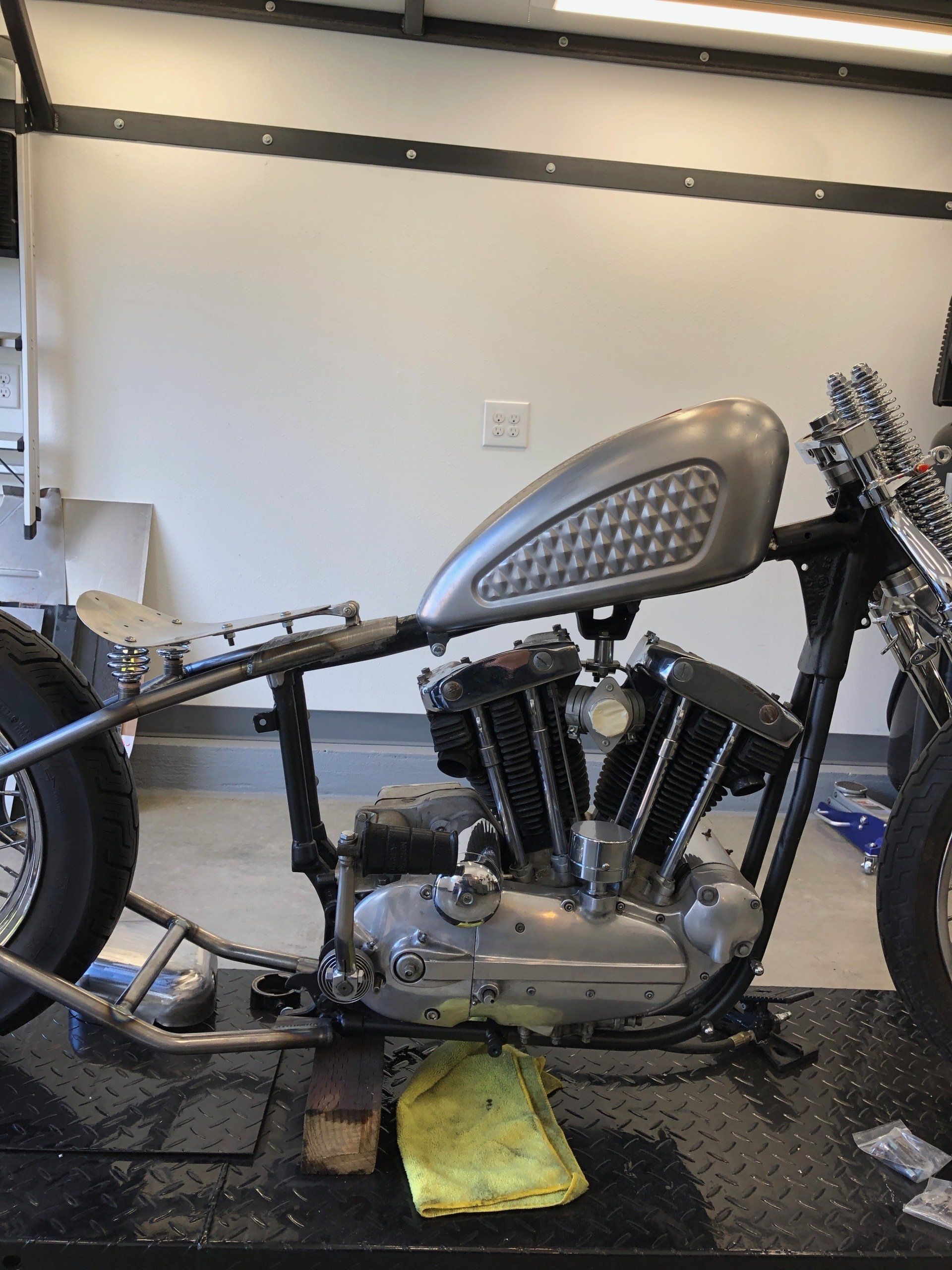 Custom chopper motorcycle frame with V-twin engine in a garage, black parts and silver tank on a lift