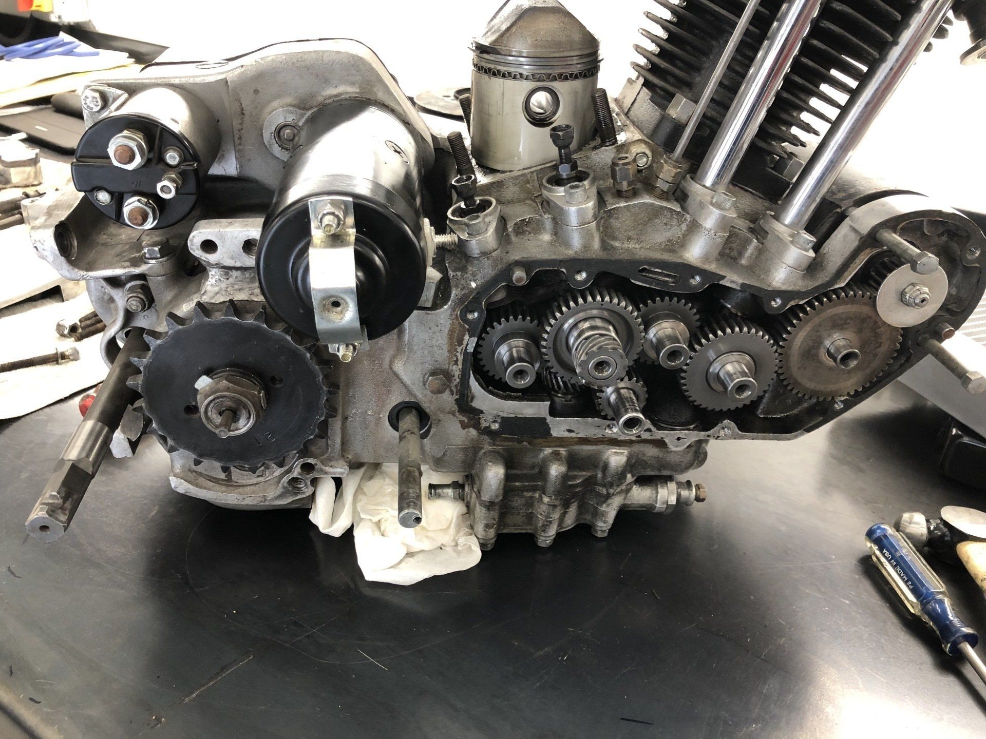 Close-up of a motorcycle engine with exposed gears and timing cover on a workbench